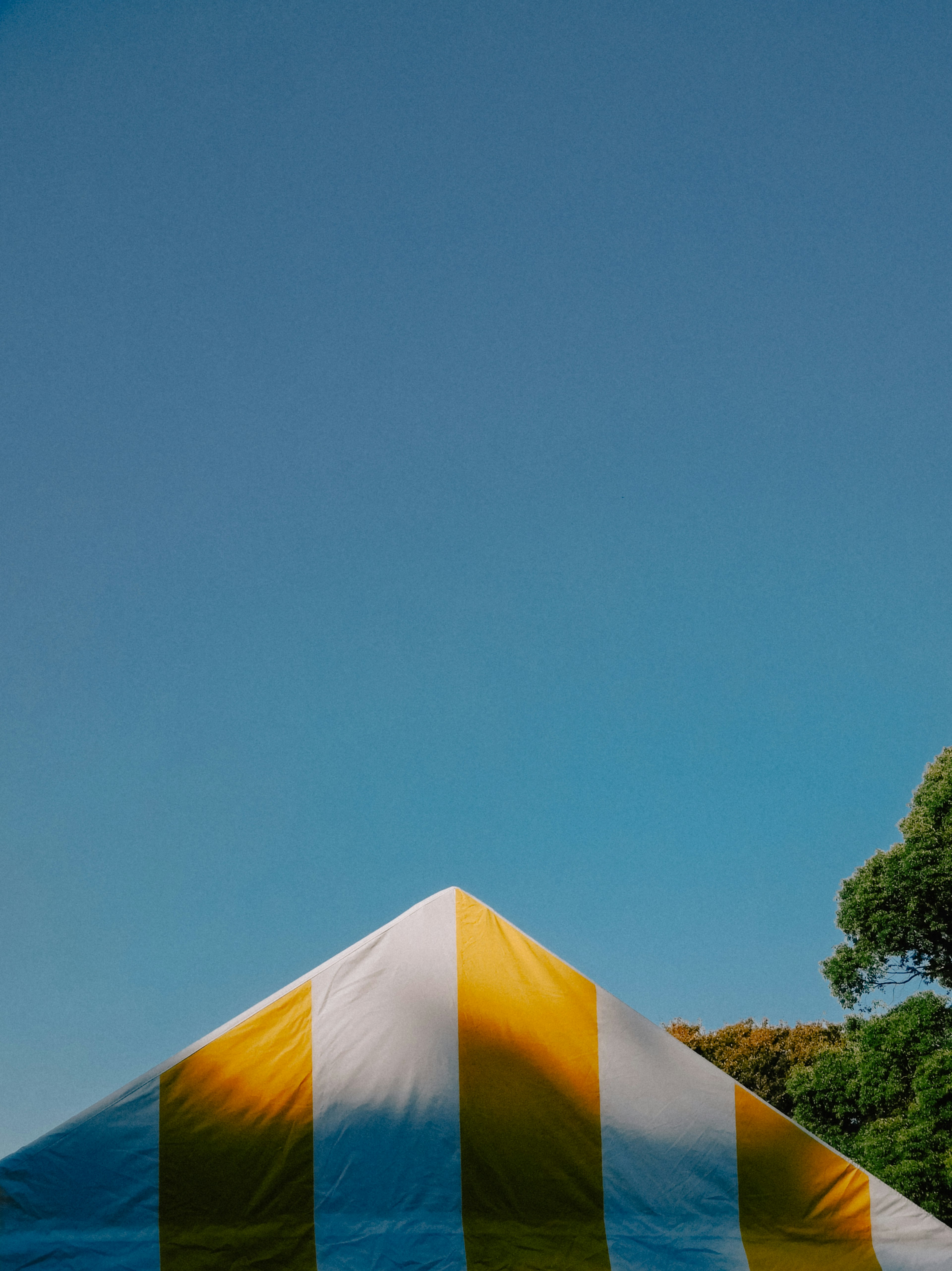 Cima de una carpa a rayas amarillas y blancas bajo un cielo azul