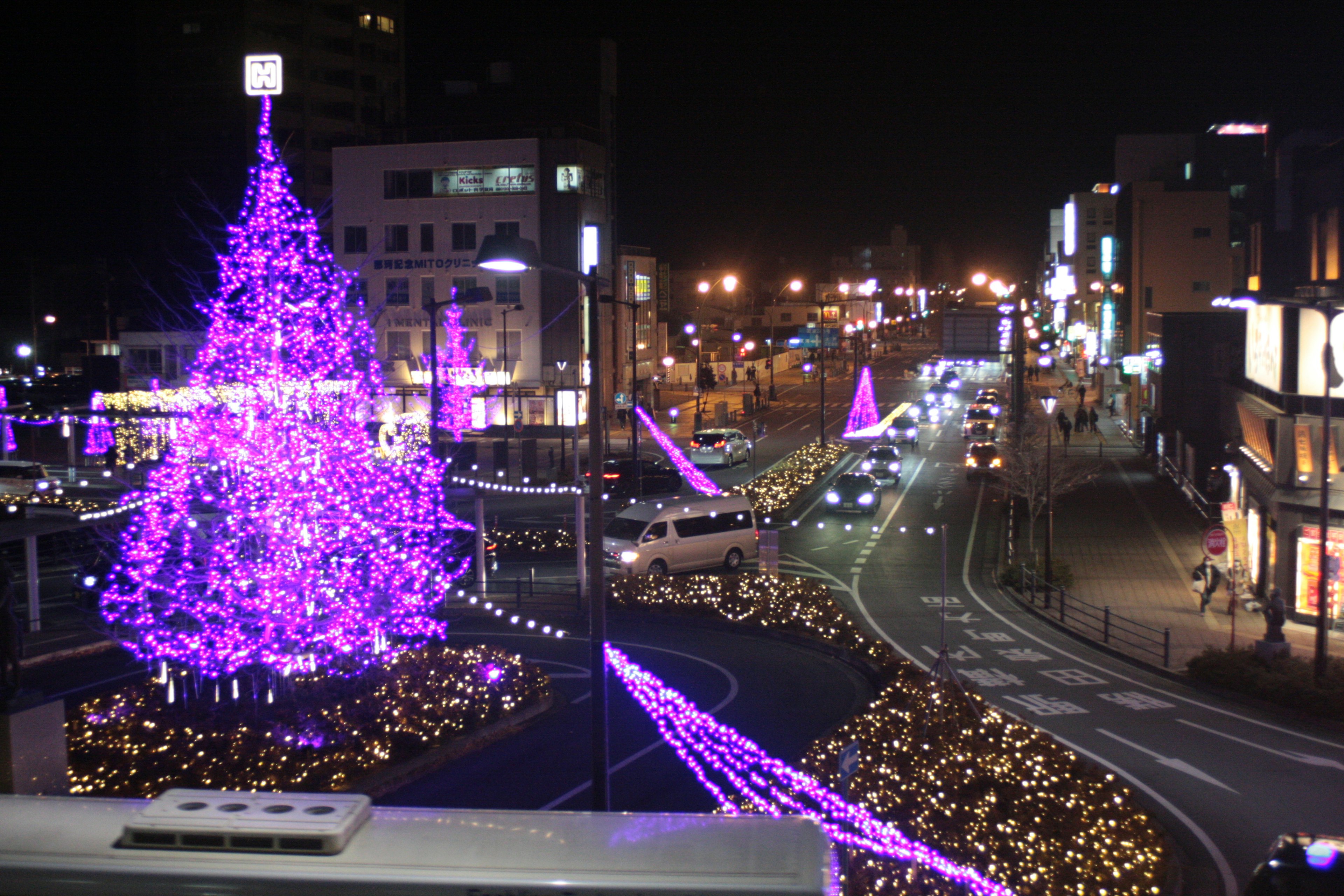 Scena notturna con un albero di Natale viola e decorazioni illuminate lungo la strada