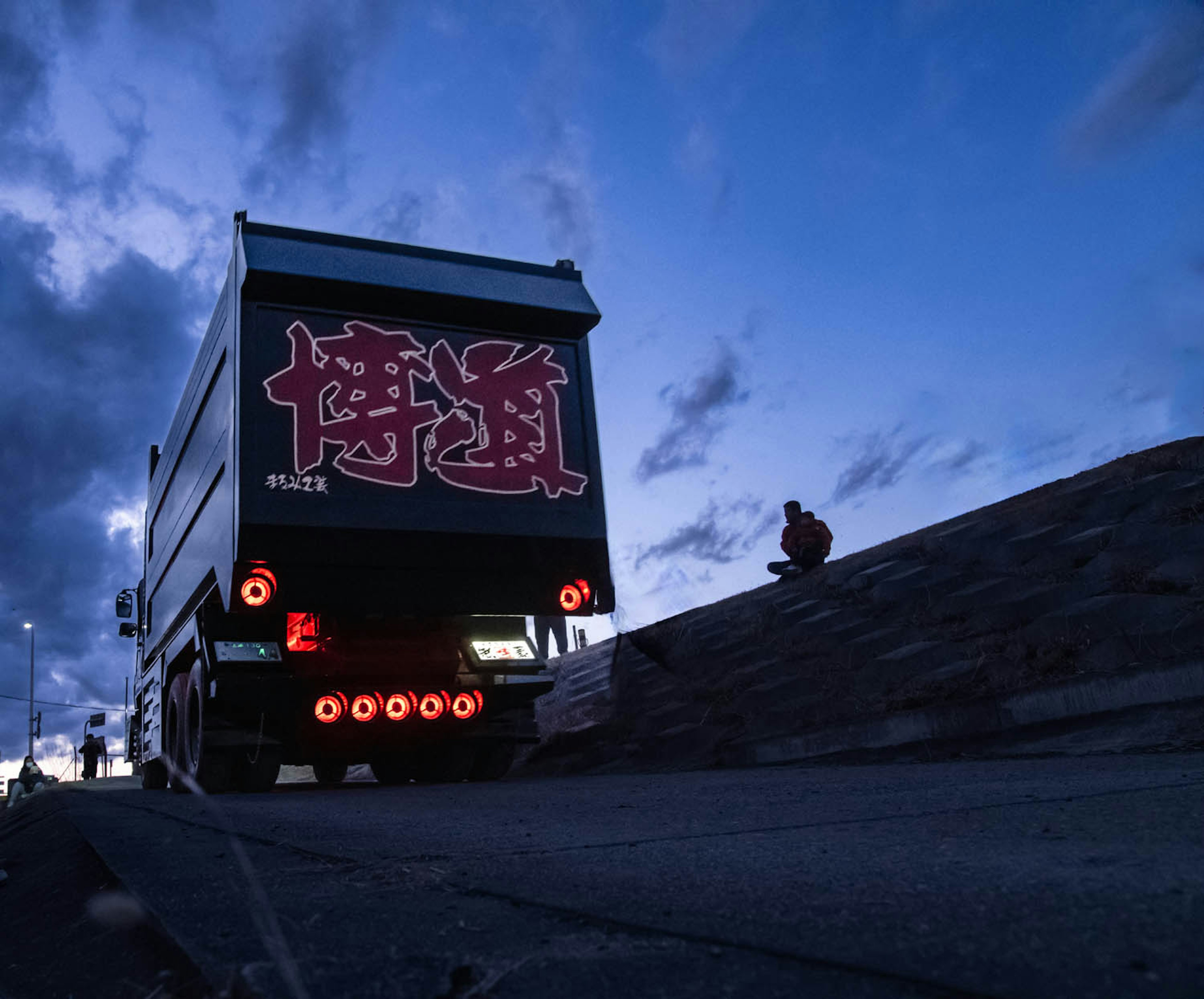 黃昏時的卡車，紅色字母和藍色天空下的人影