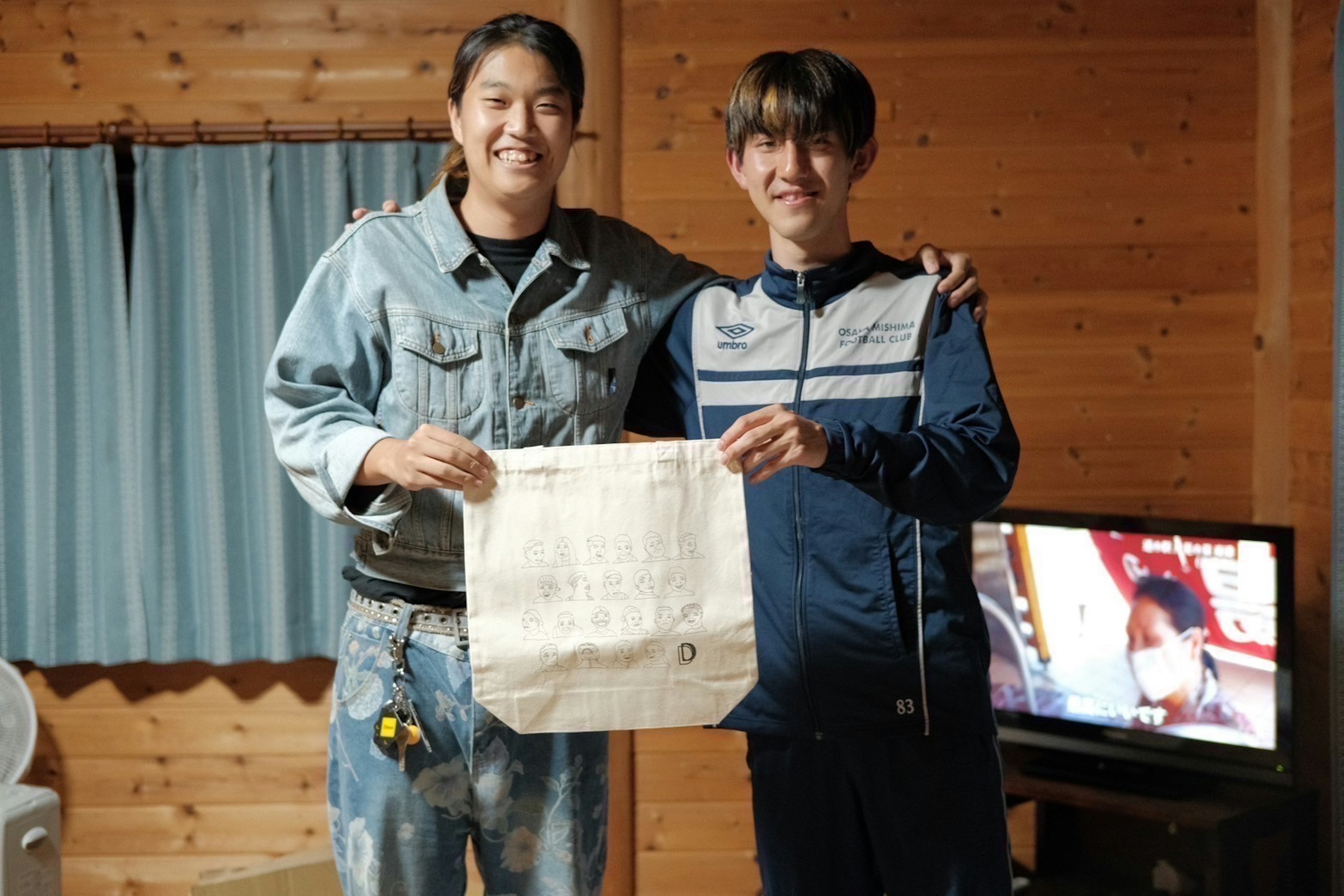 Two young men smiling while holding a piece of paper with a wooden wall background