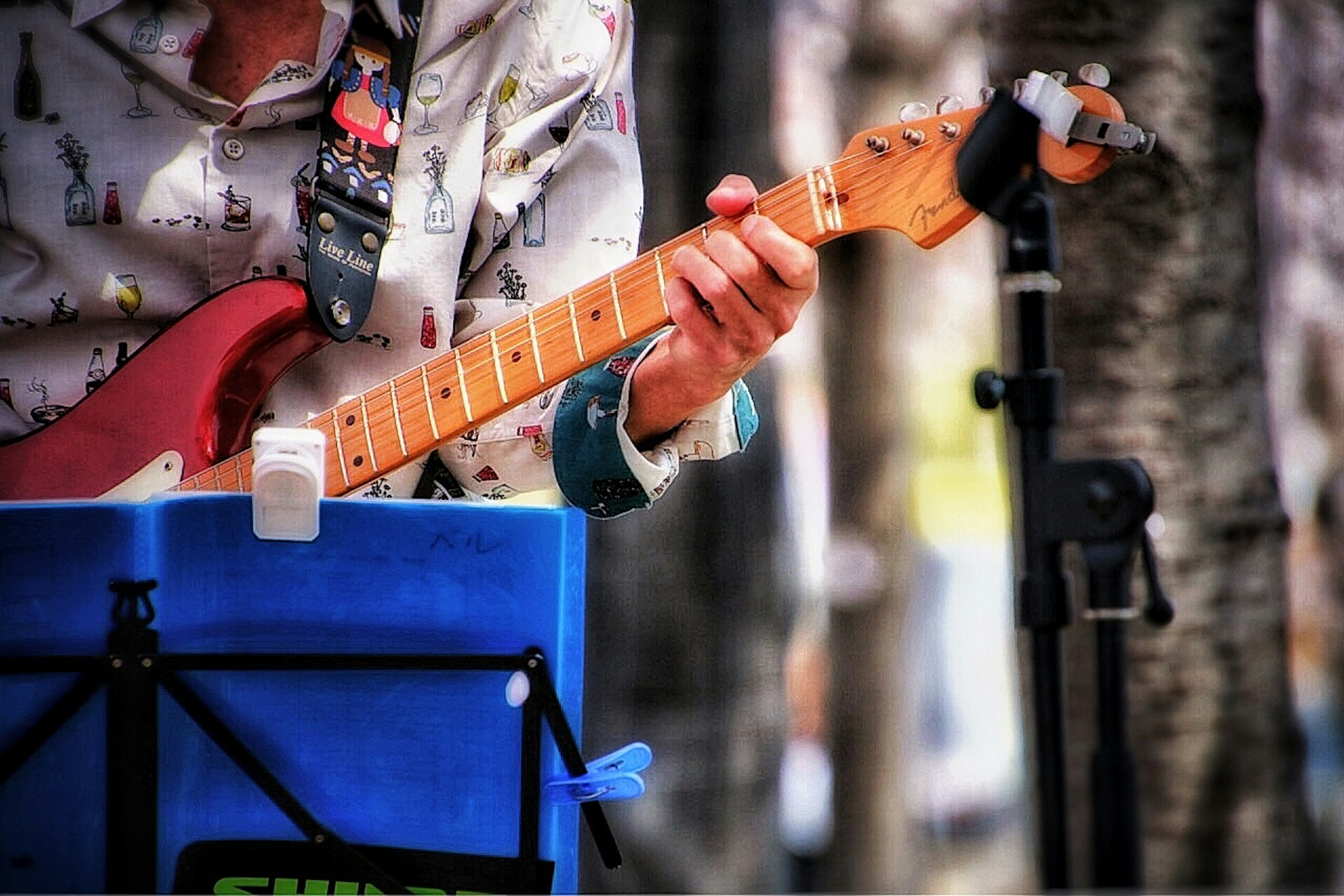 Close-up of a man's hand playing a red electric guitar with a blue music stand