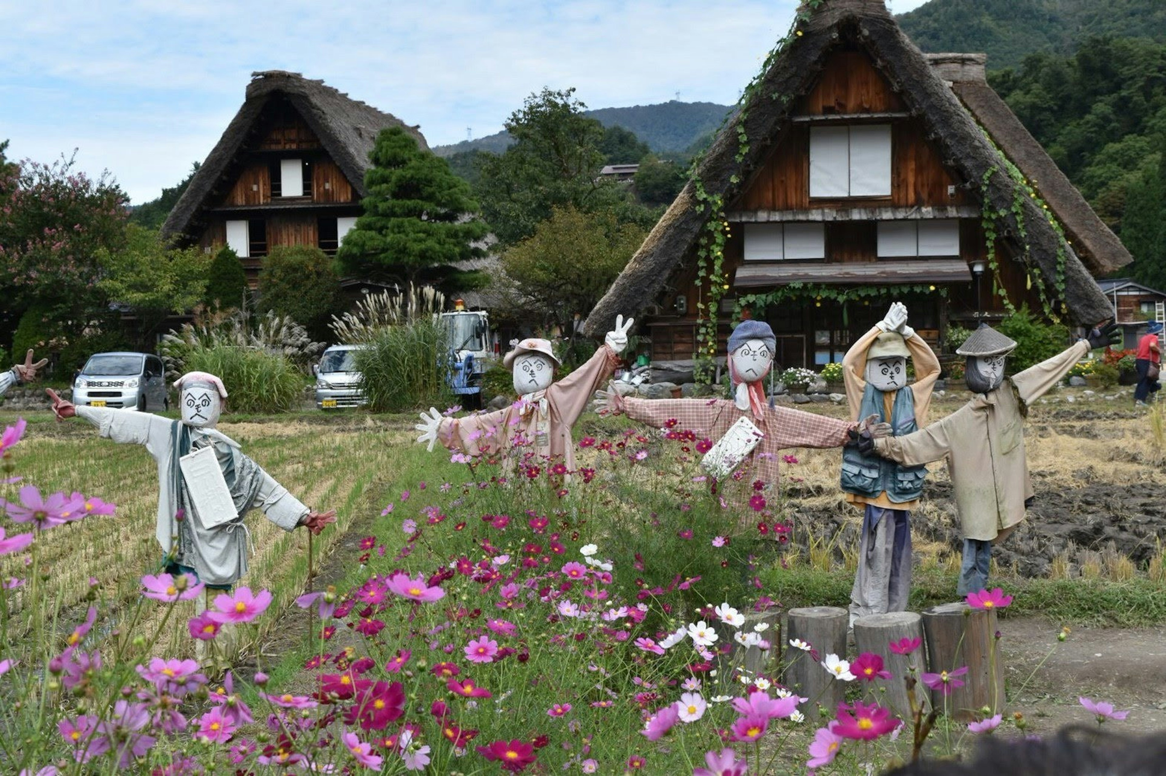 Vogelscheuchen vor traditionellen Gassho-Zukuri-Häusern umgeben von Blumen