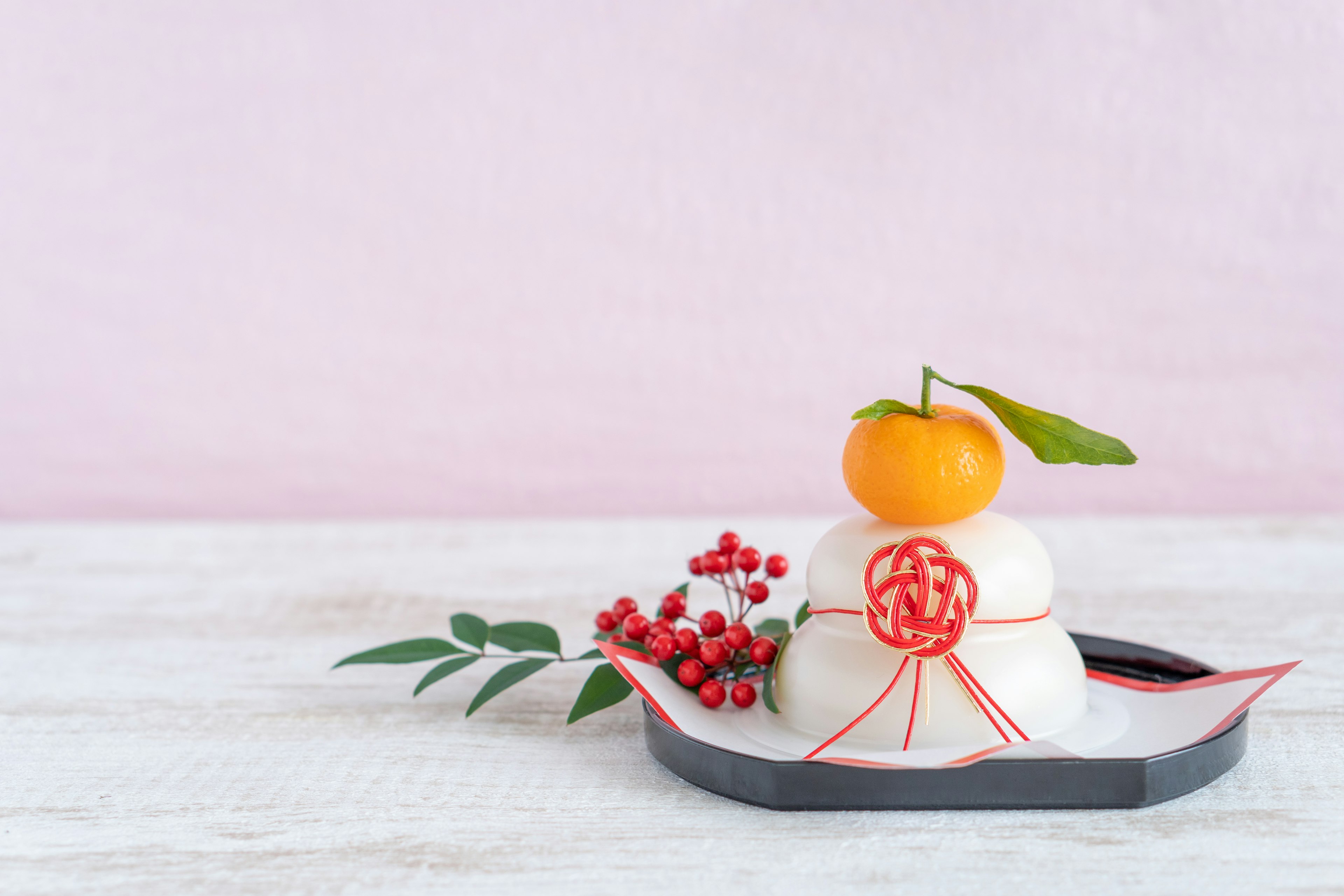 Traditional Japanese decoration featuring white mochi topped with a mandarin and leaf surrounded by red berry accents