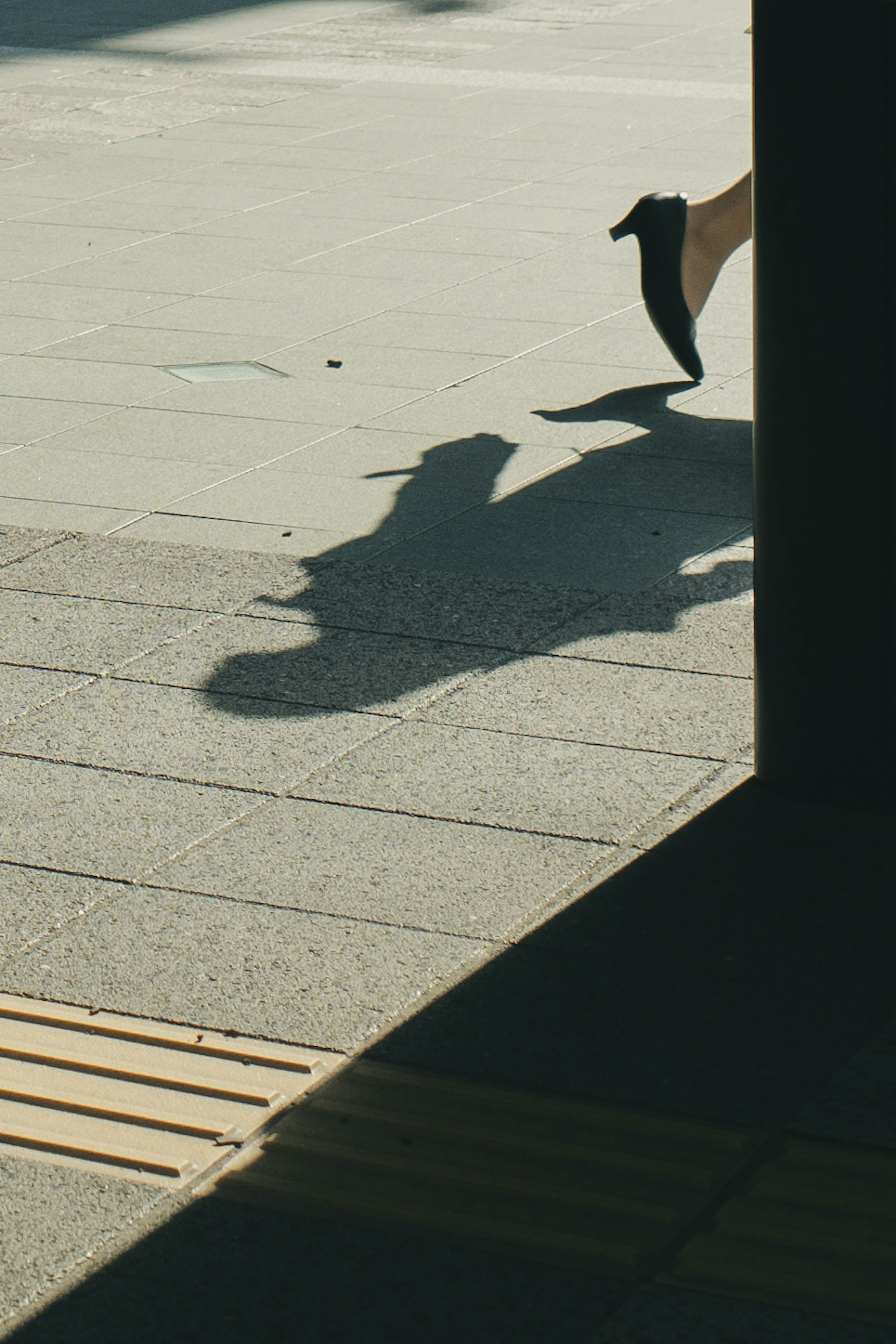 Un pied dans une chaussure à talon haut projetant une ombre sur le pavé