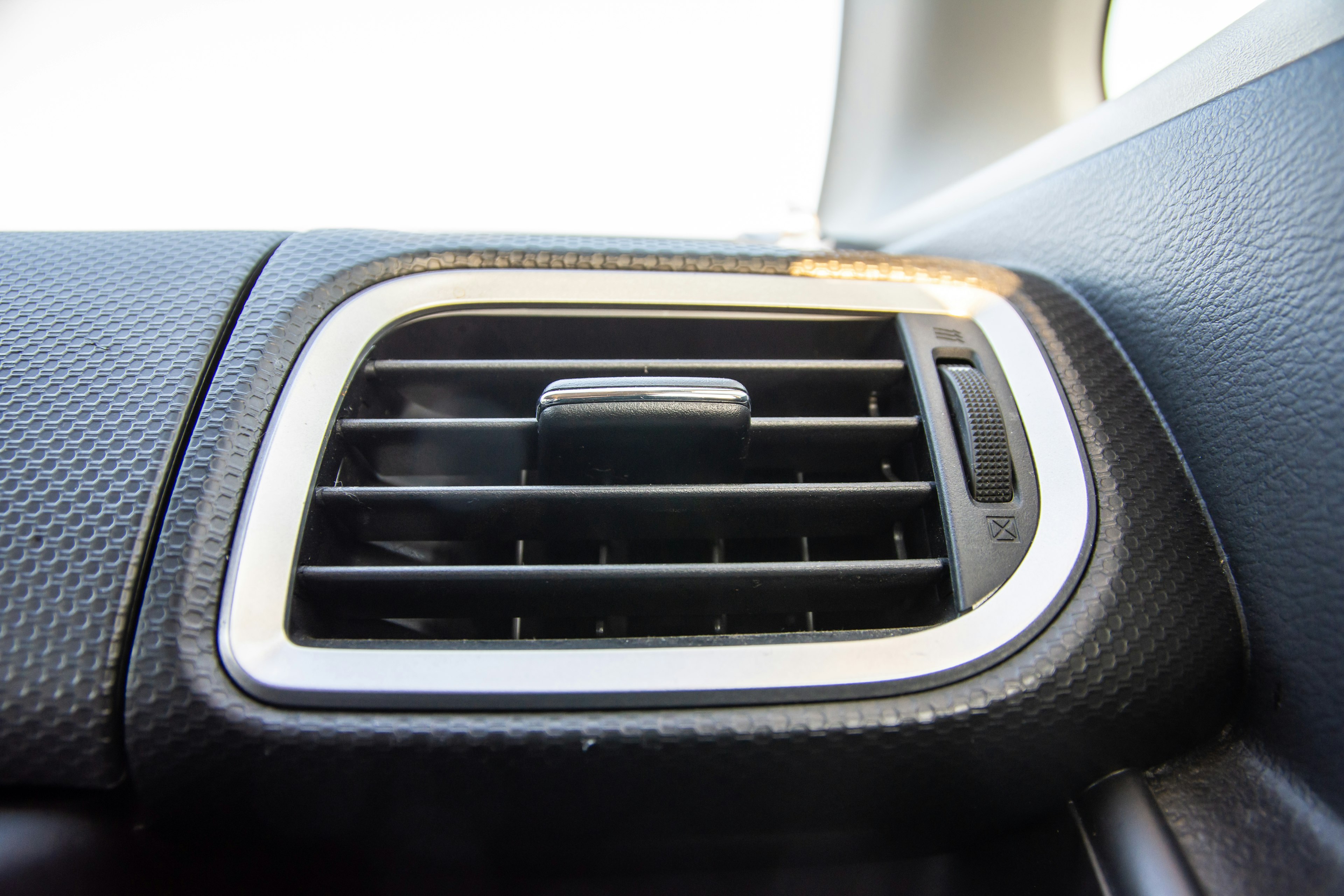 Gros plan d'une grille de climatisation de voiture avec un cadre argenté et une grille noire