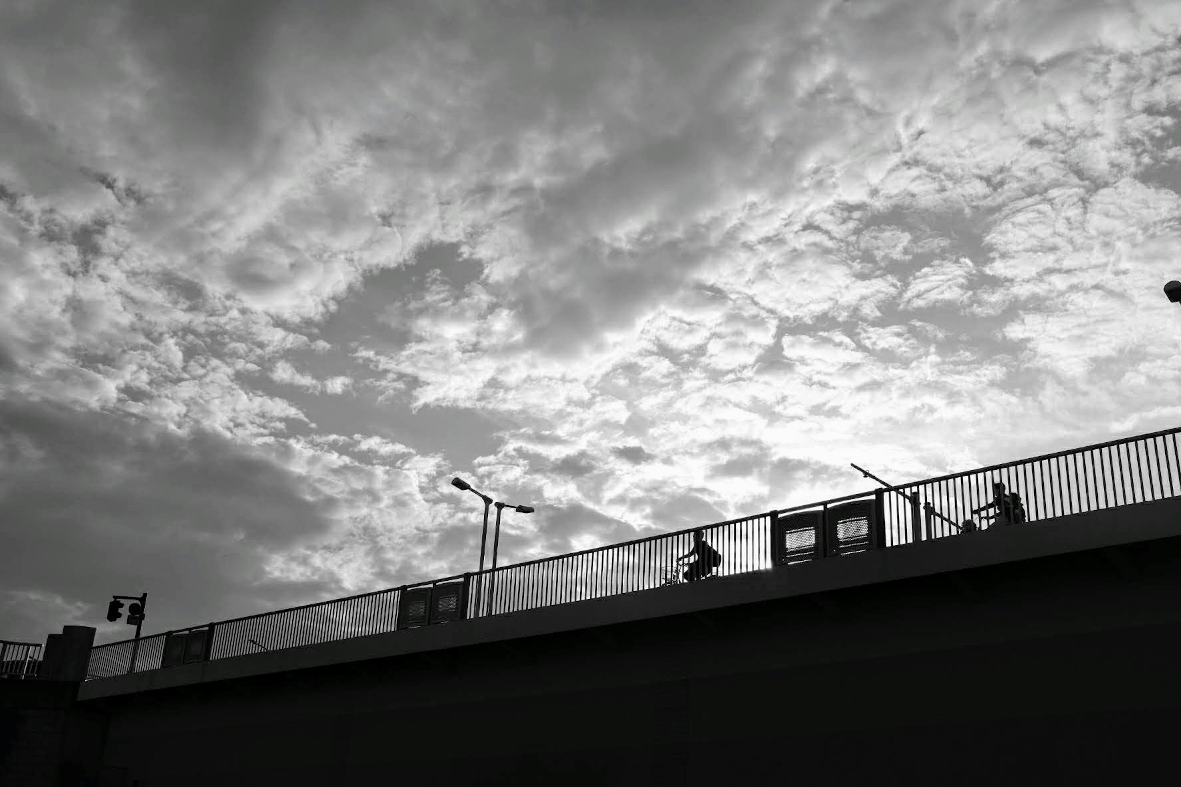 白黒の空とシルエットの人々が映る橋の風景