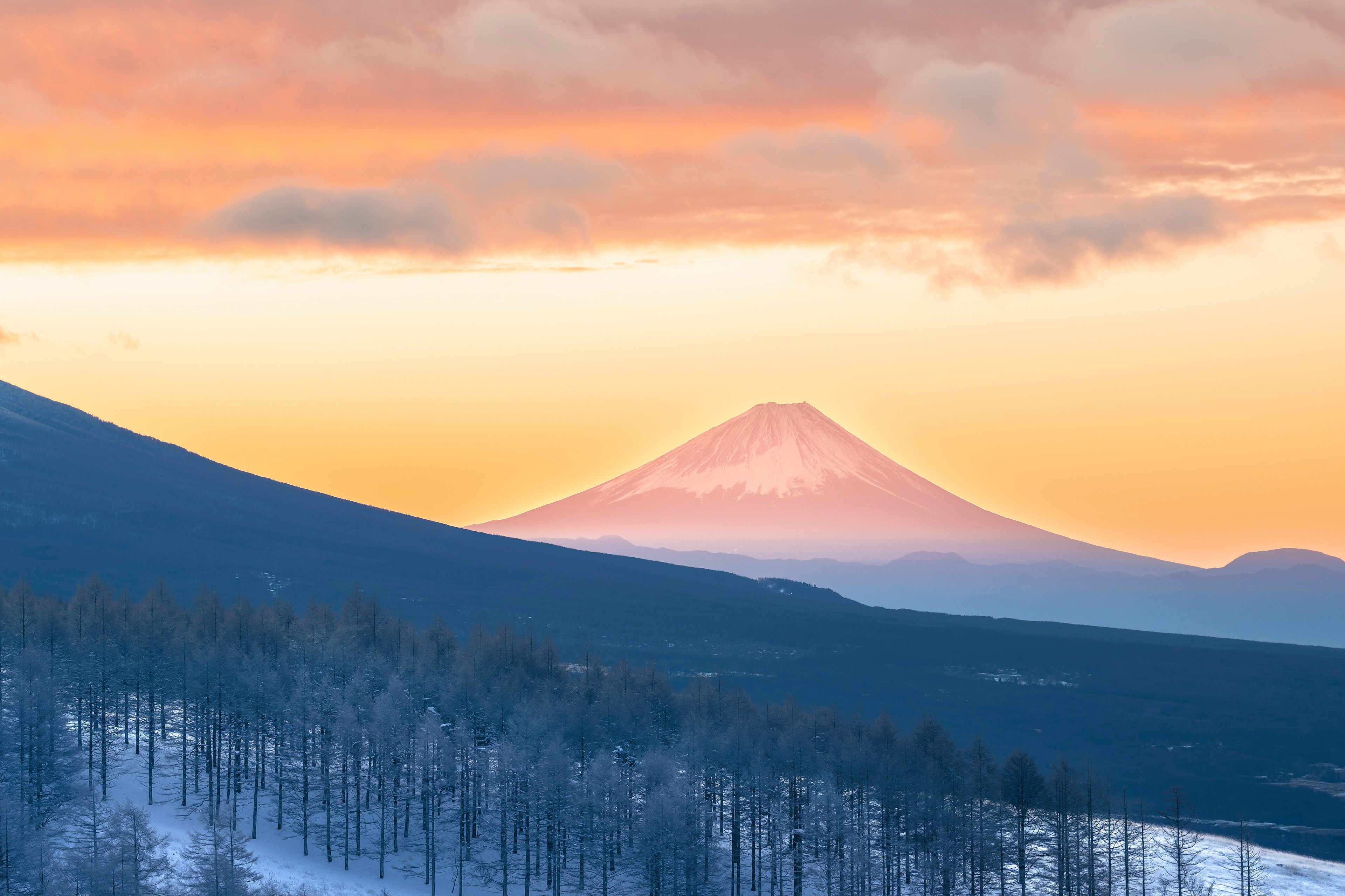 雪に覆われた山々と美しい夕焼けの下にそびえる富士山