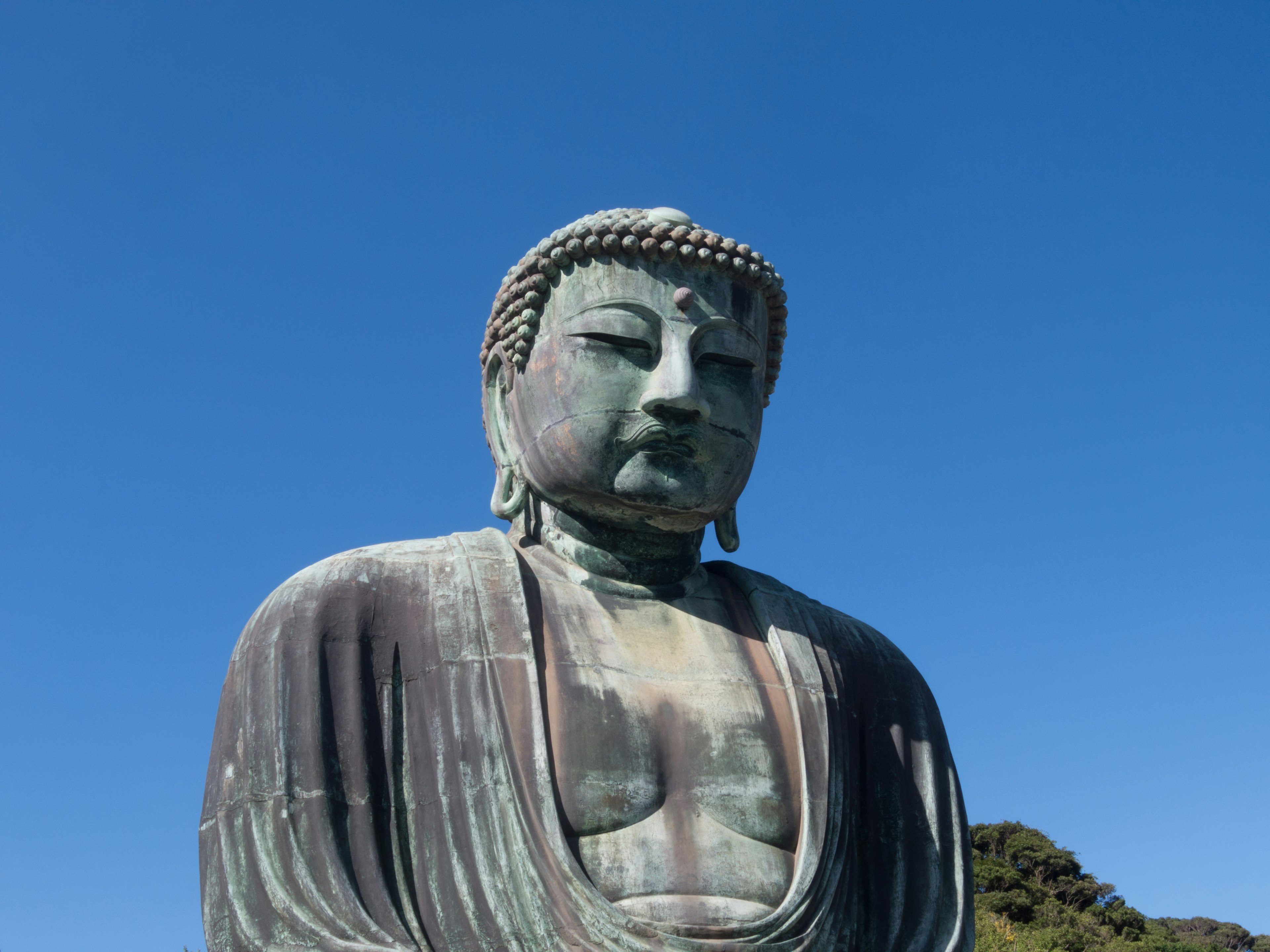 A large Buddha statue under a clear blue sky, serene expression, intricate details prominent