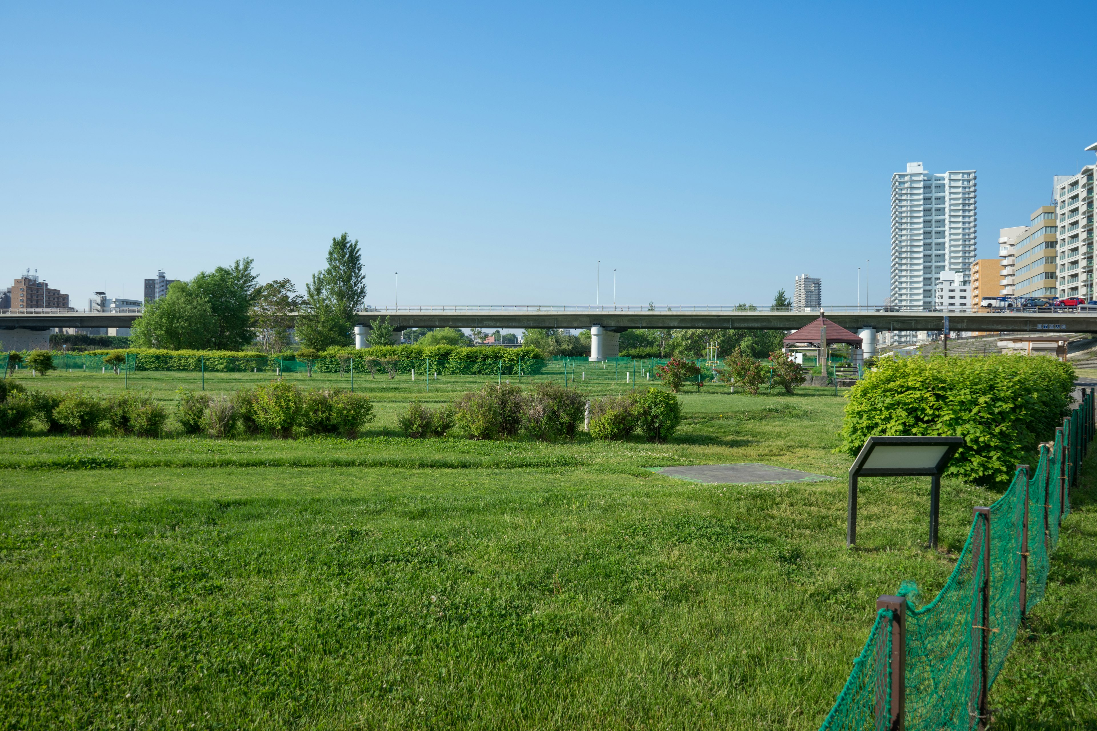 Espace vert large sous un ciel bleu avec un pont et des immeubles