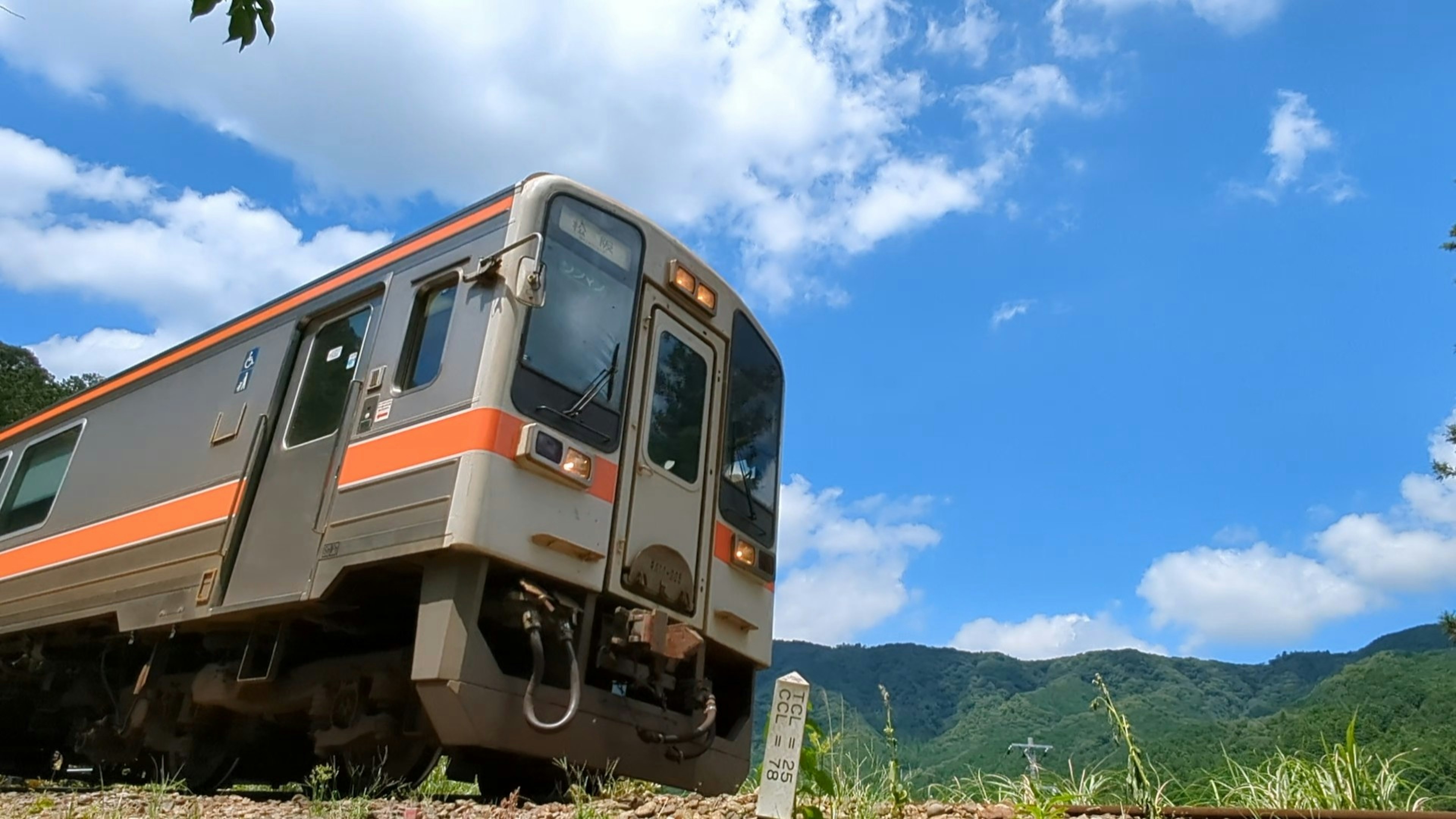 青空の下で走るオレンジのストライプの列車と山々