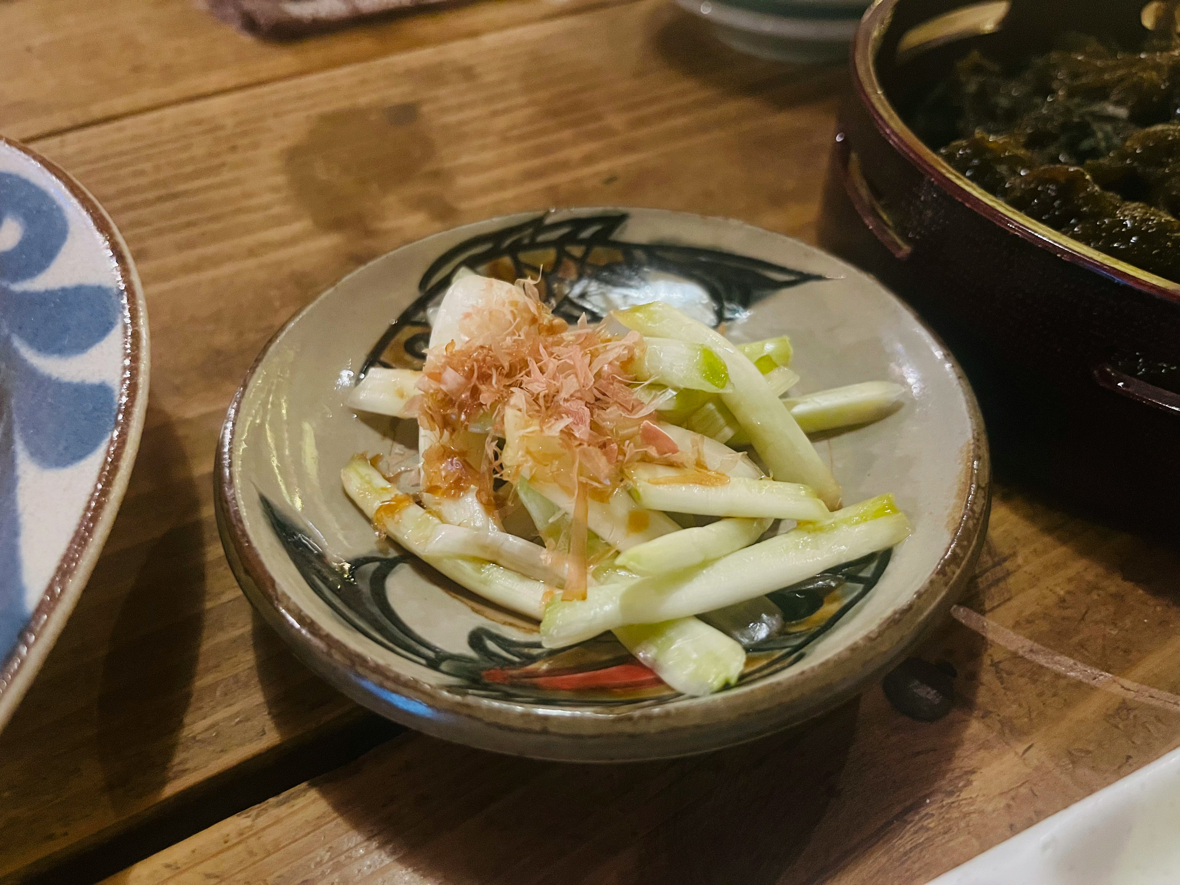 Un plato pequeño con verduras en rodajas finas cubiertas con copos de bonito