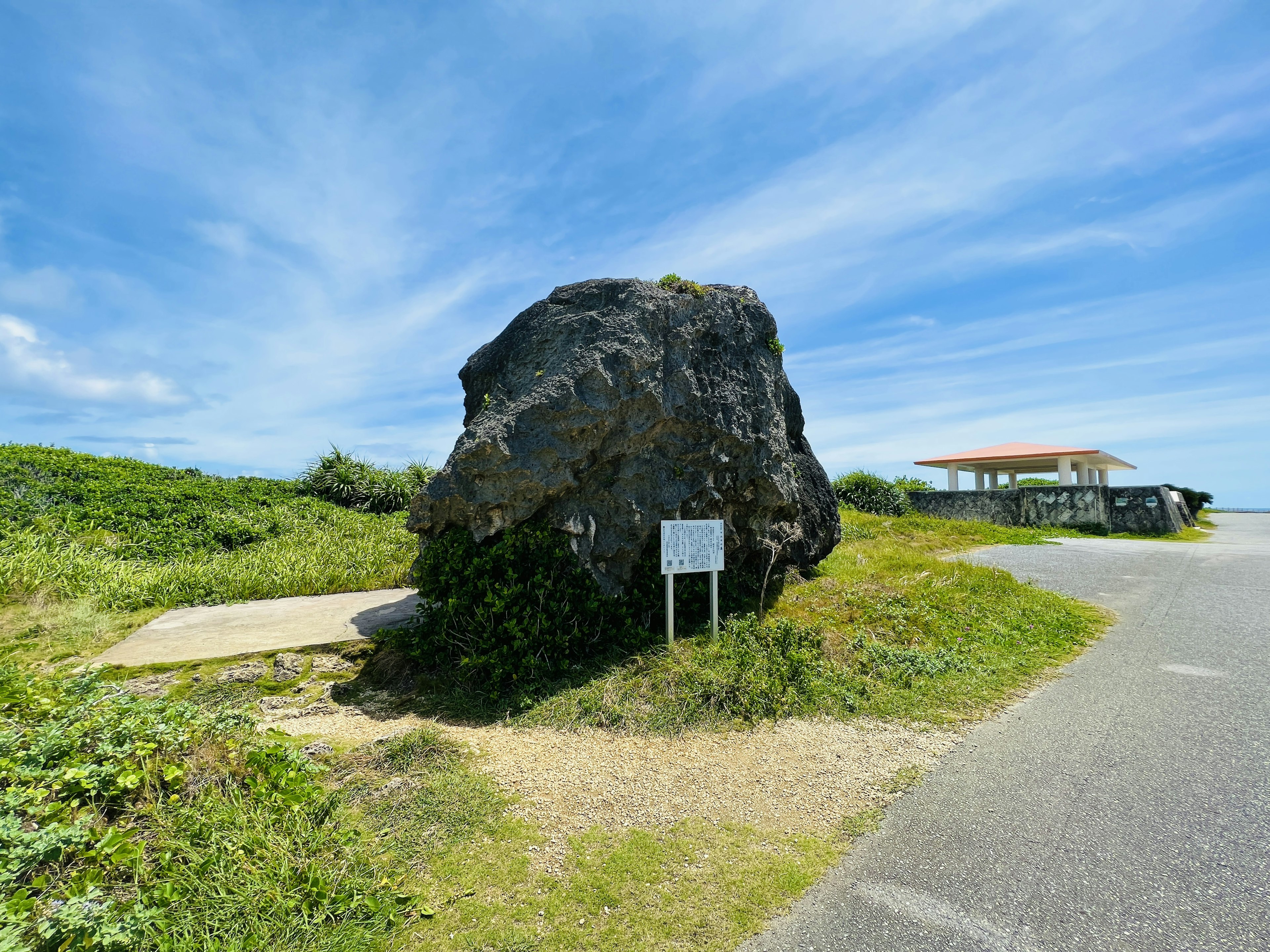 Grande roche sous un ciel bleu clair avec un panneau à proximité