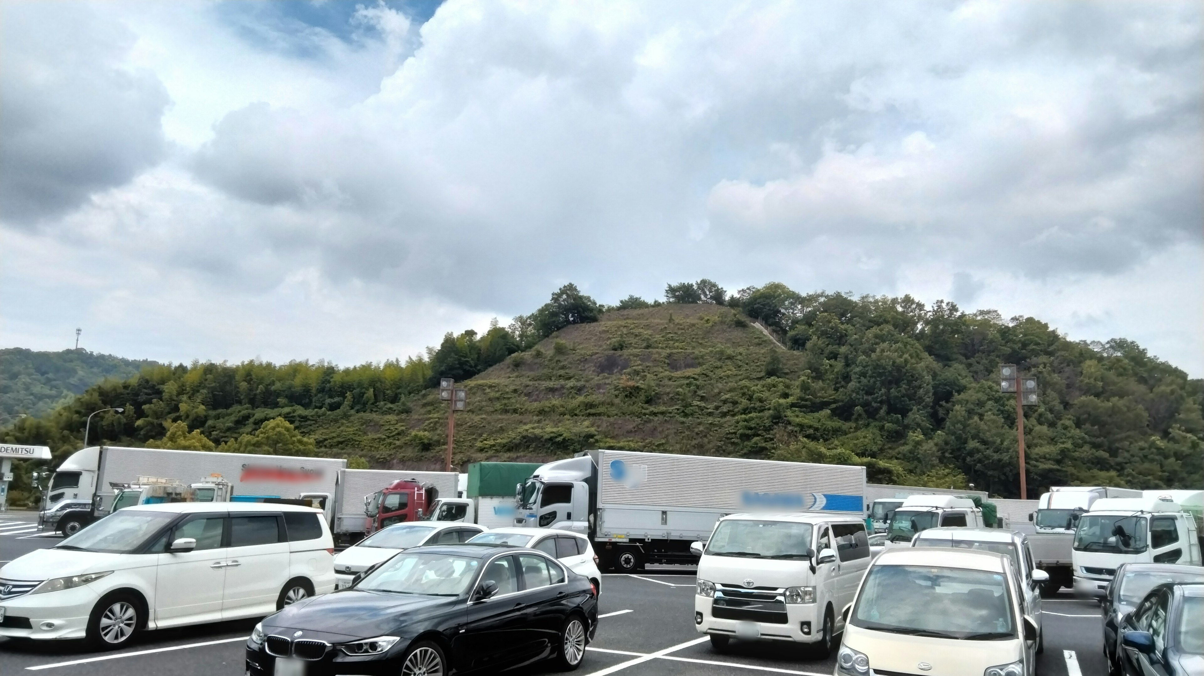 Many cars parked in a lot with a hill in the background