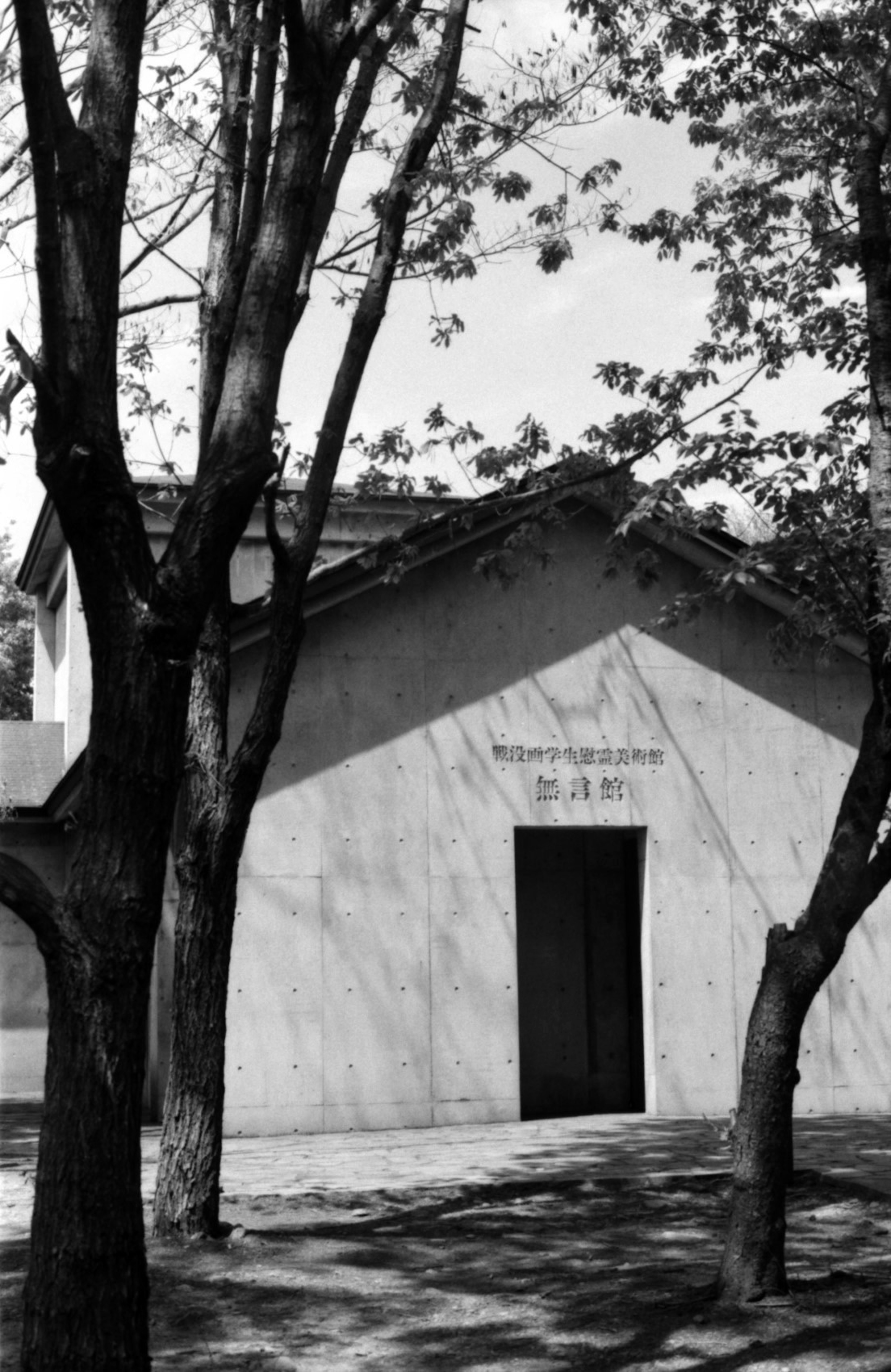 Immagine in bianco e nero di un edificio con alberi intorno e testo sopra l'ingresso