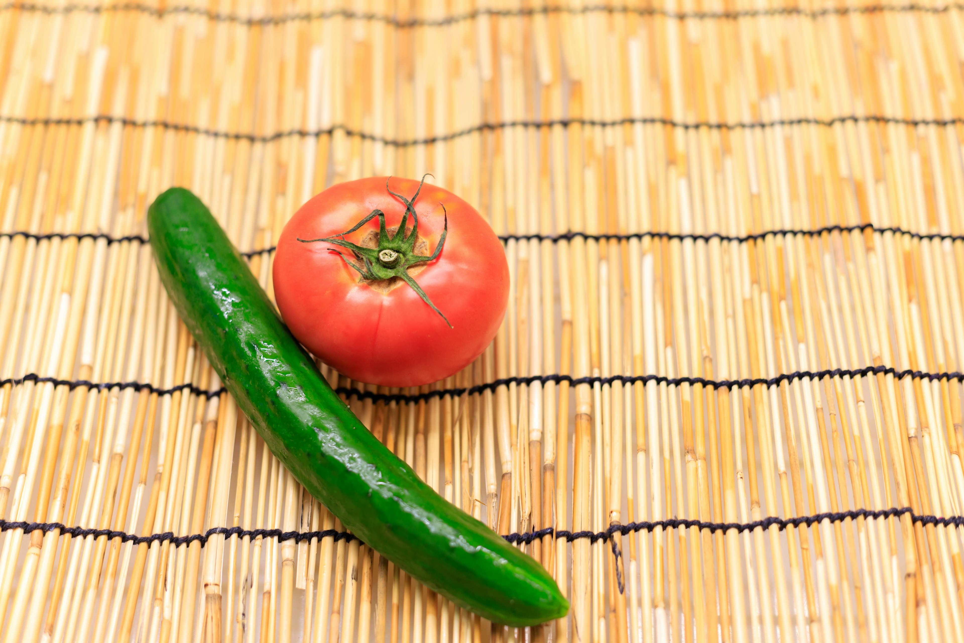 A red tomato and a green cucumber placed on a bamboo mat