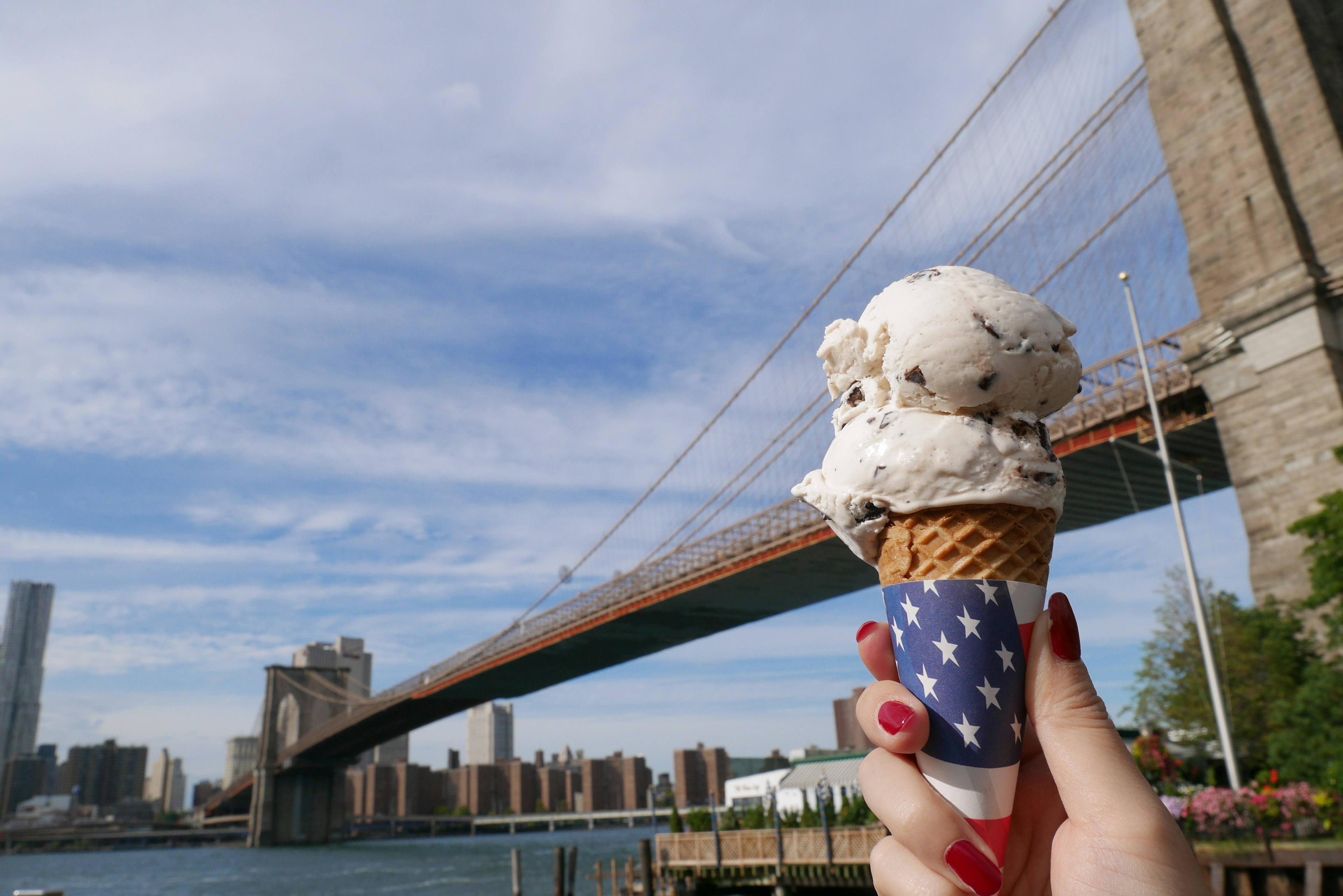 Mano che tiene un cono gelato con il ponte di Brooklyn sullo sfondo