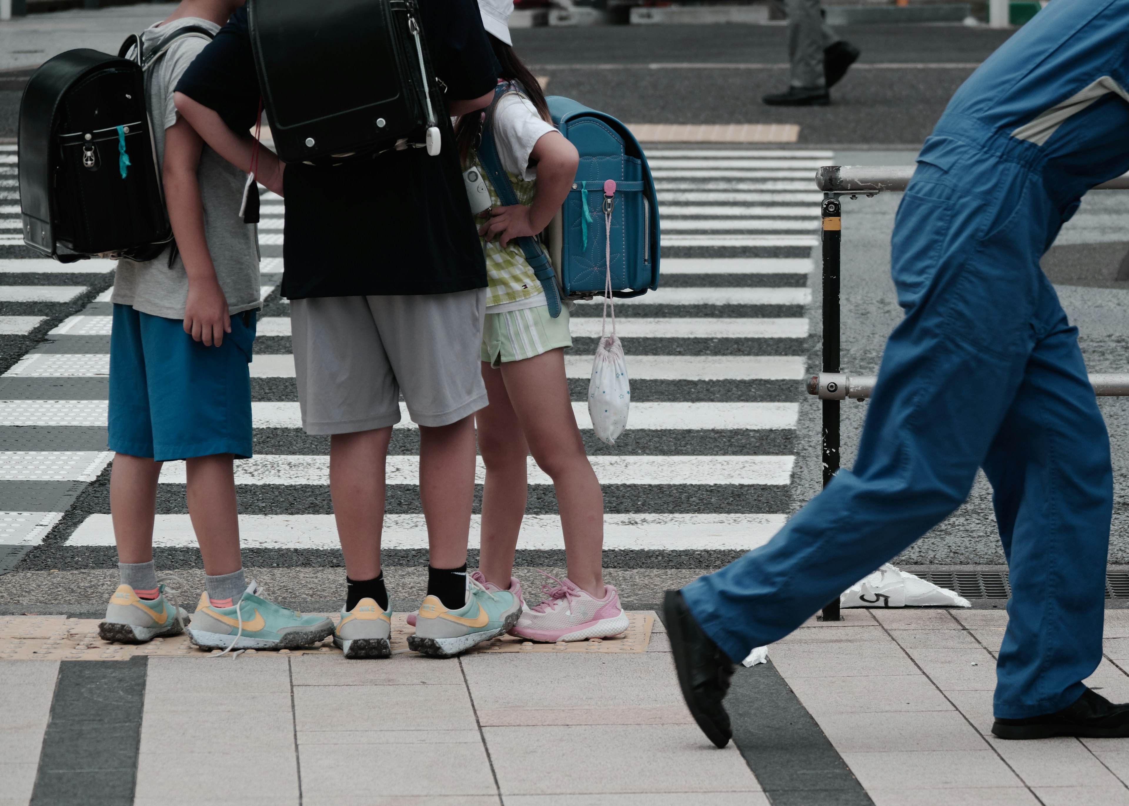 Niños esperando en un cruce peatonal con una persona con ropa de trabajo azul pasando