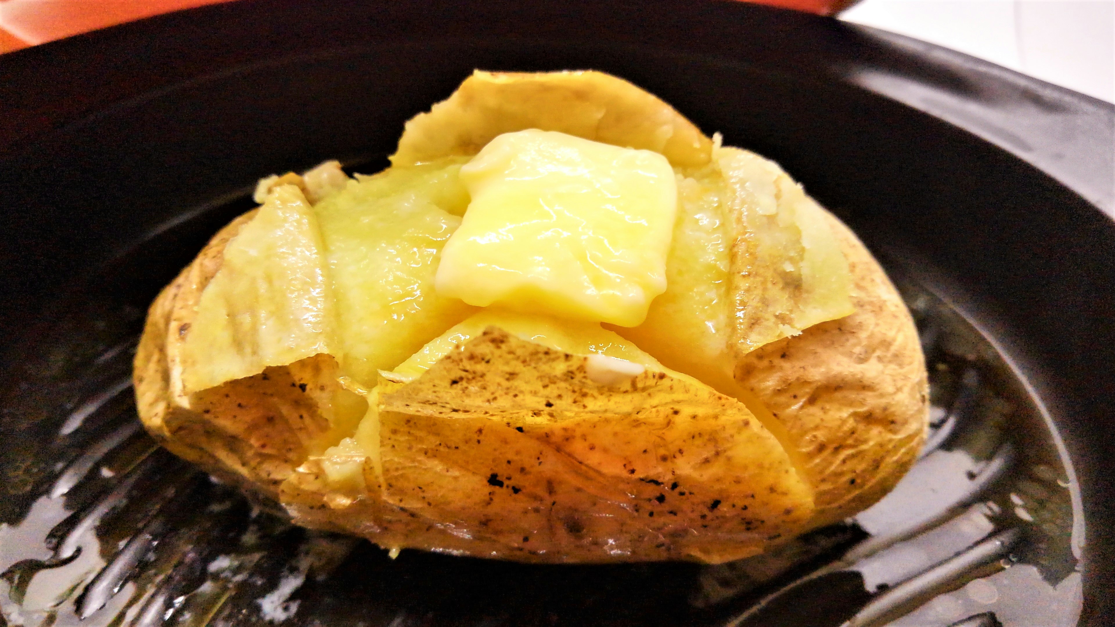 Baked potato topped with butter on a black plate