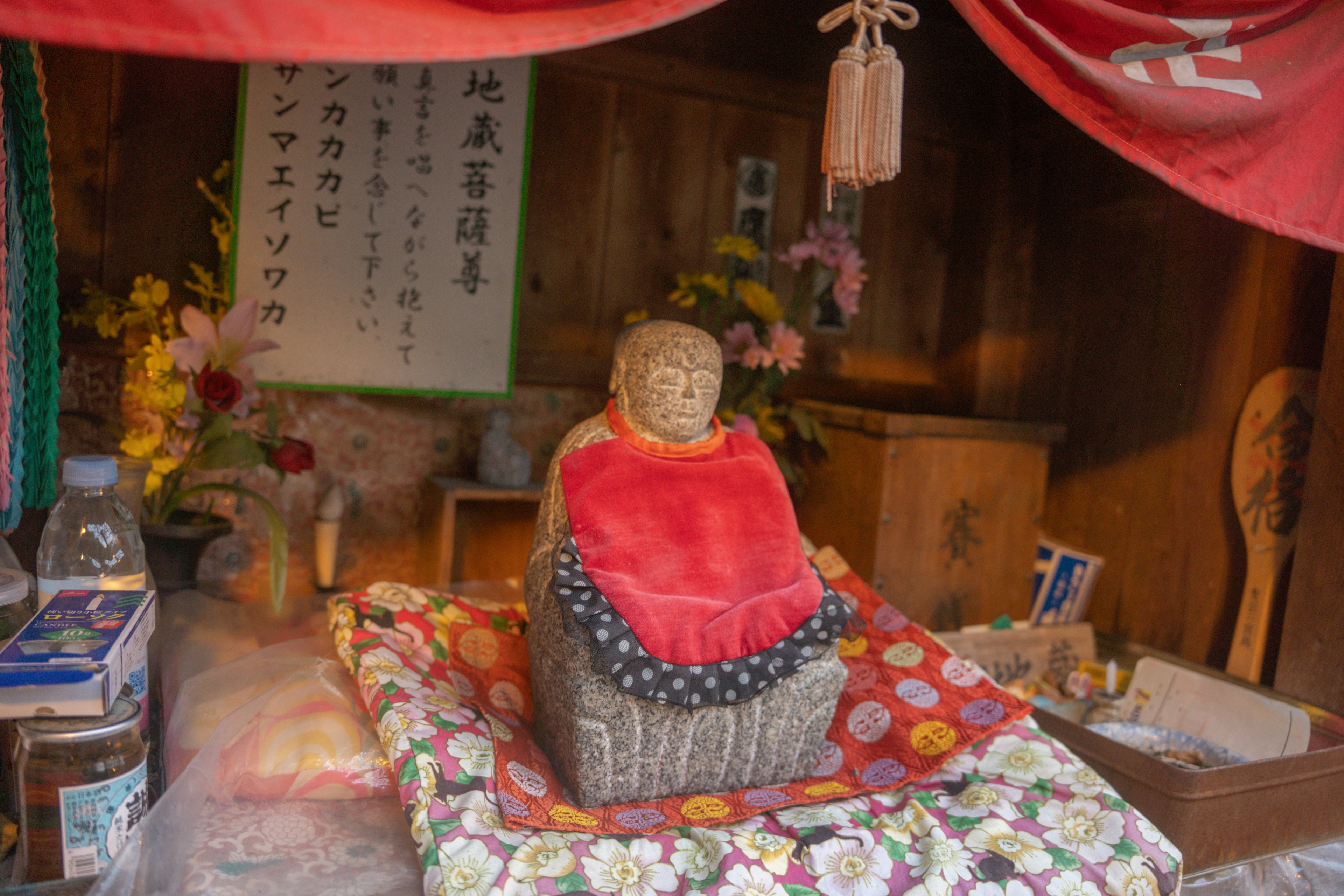 Un pequeño santuario con una estatua de Buda cubierta rodeada de flores y ofrendas