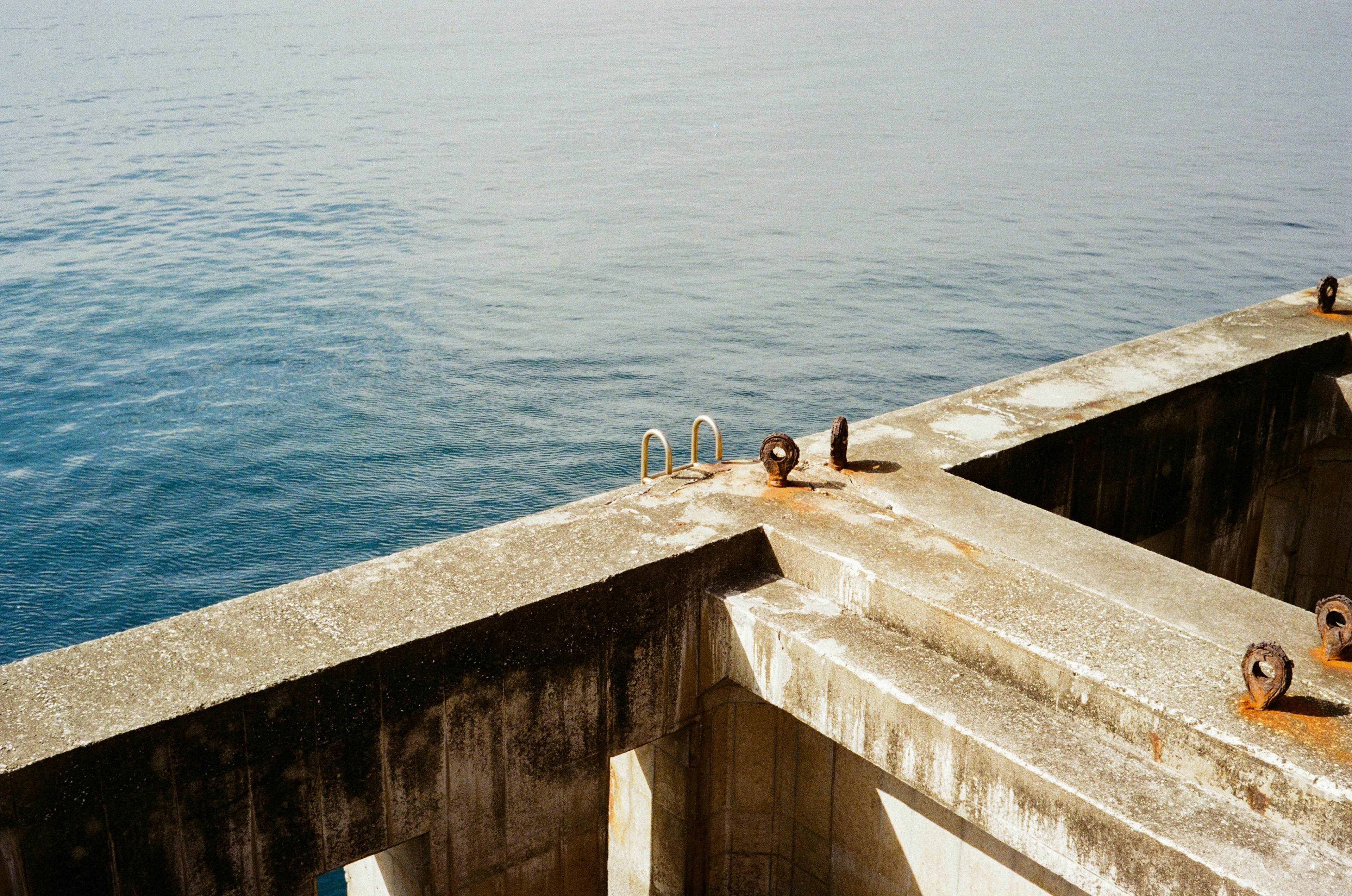 Concrete pier with metal rings and rusty fasteners overlooking the calm sea