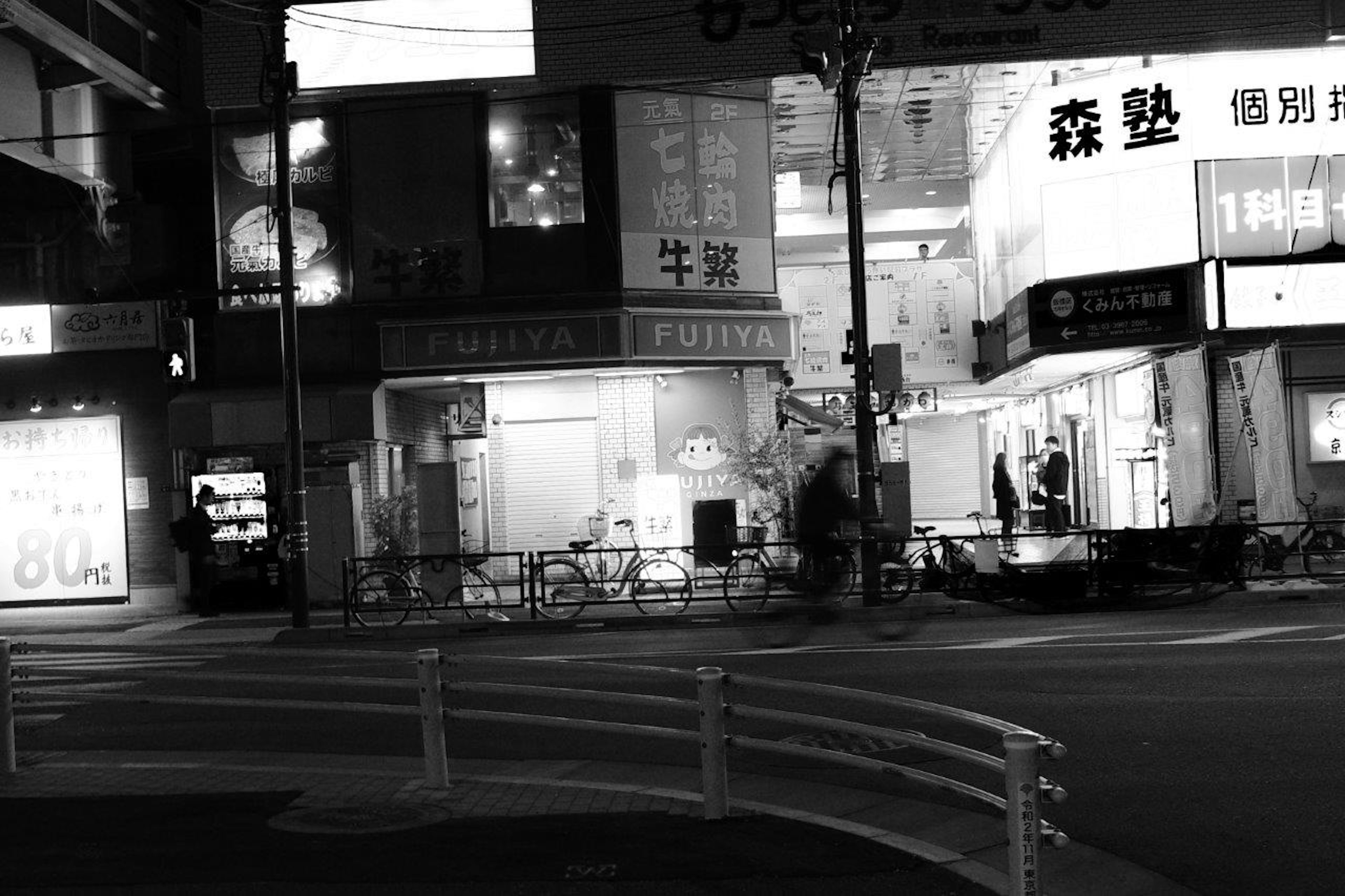 Black and white photo of a street corner with shop signs and bicycles