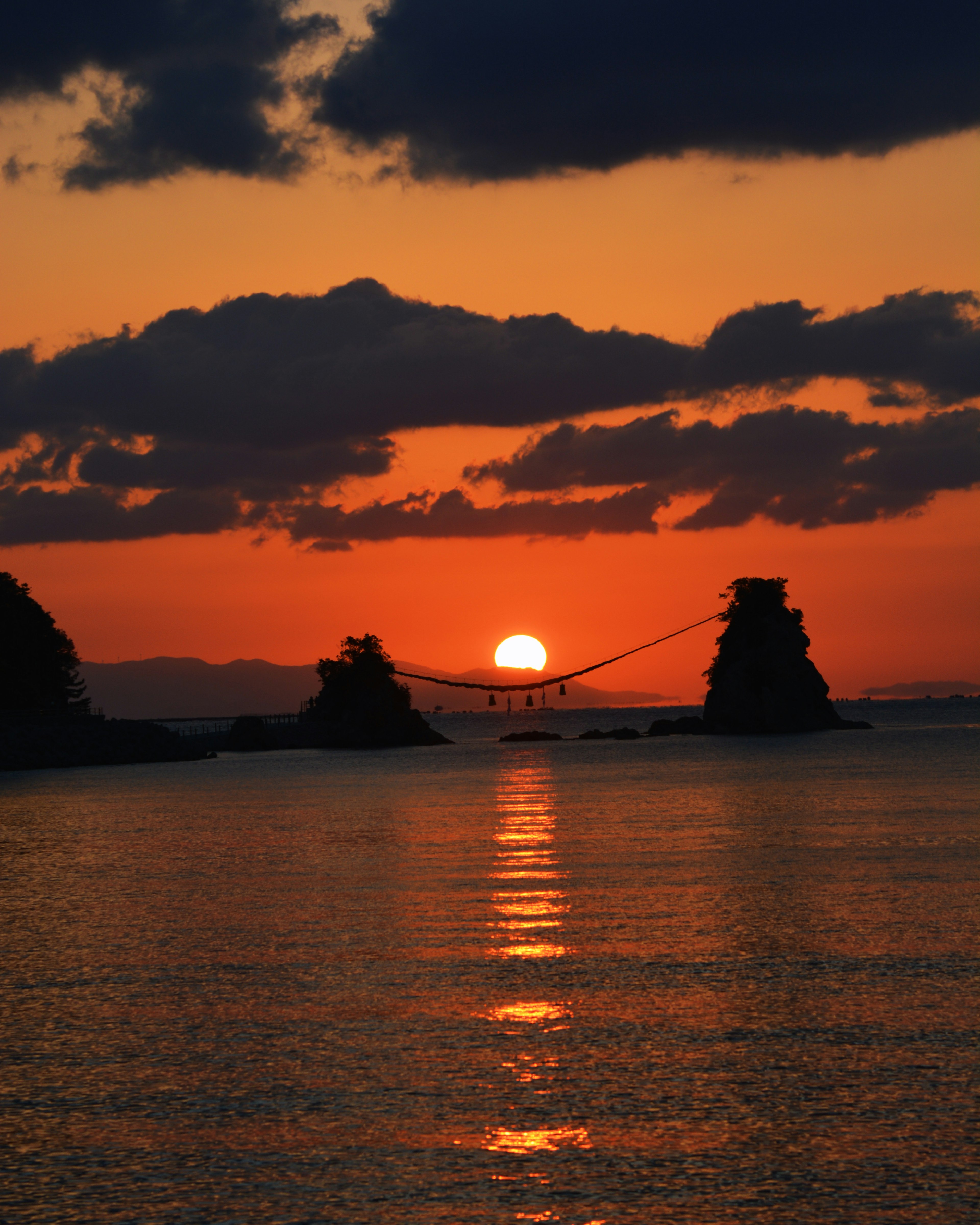 Hermoso paisaje de un atardecer sobre el mar con rocas en silueta y un puente