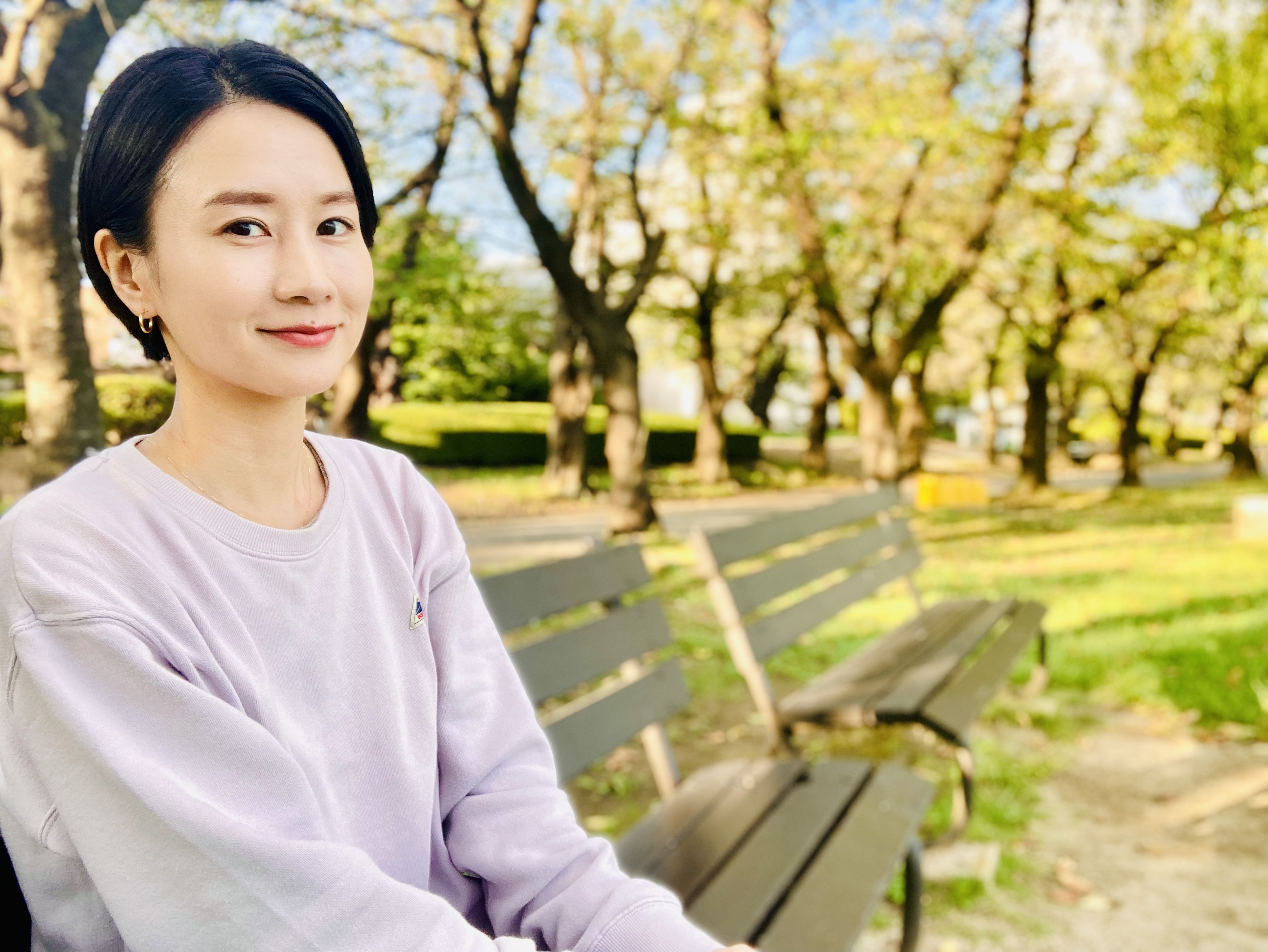 微笑的女性坐在公園長椅上周圍環繞著樹木