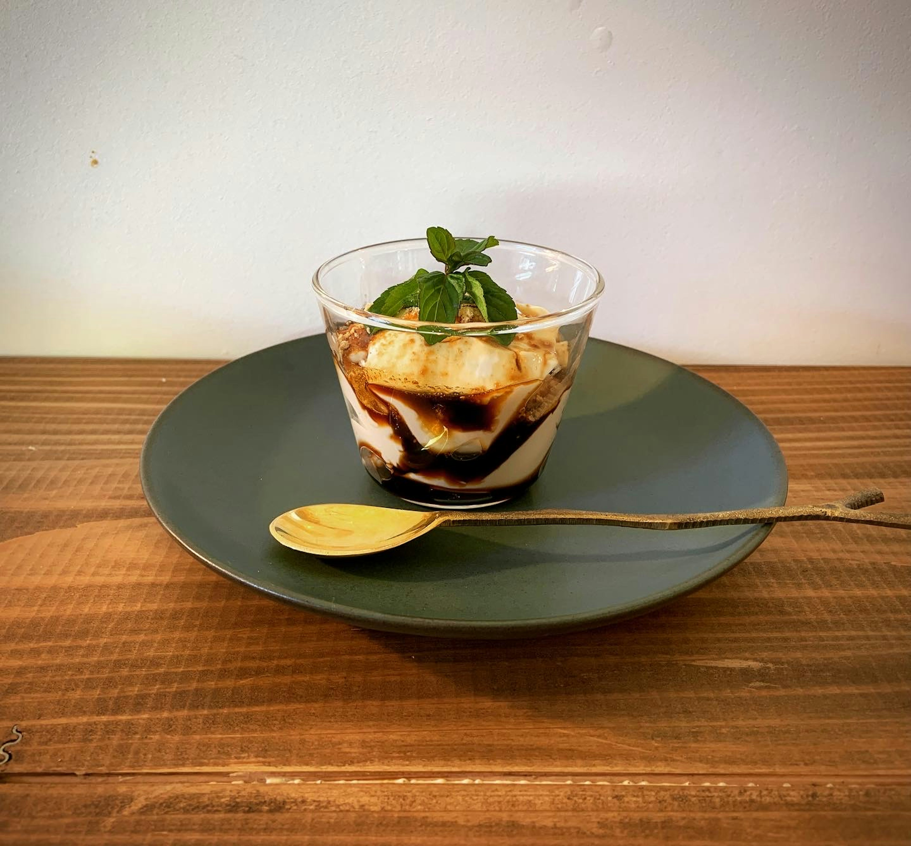 Dessert in a glass cup topped with cream and banana on a green plate