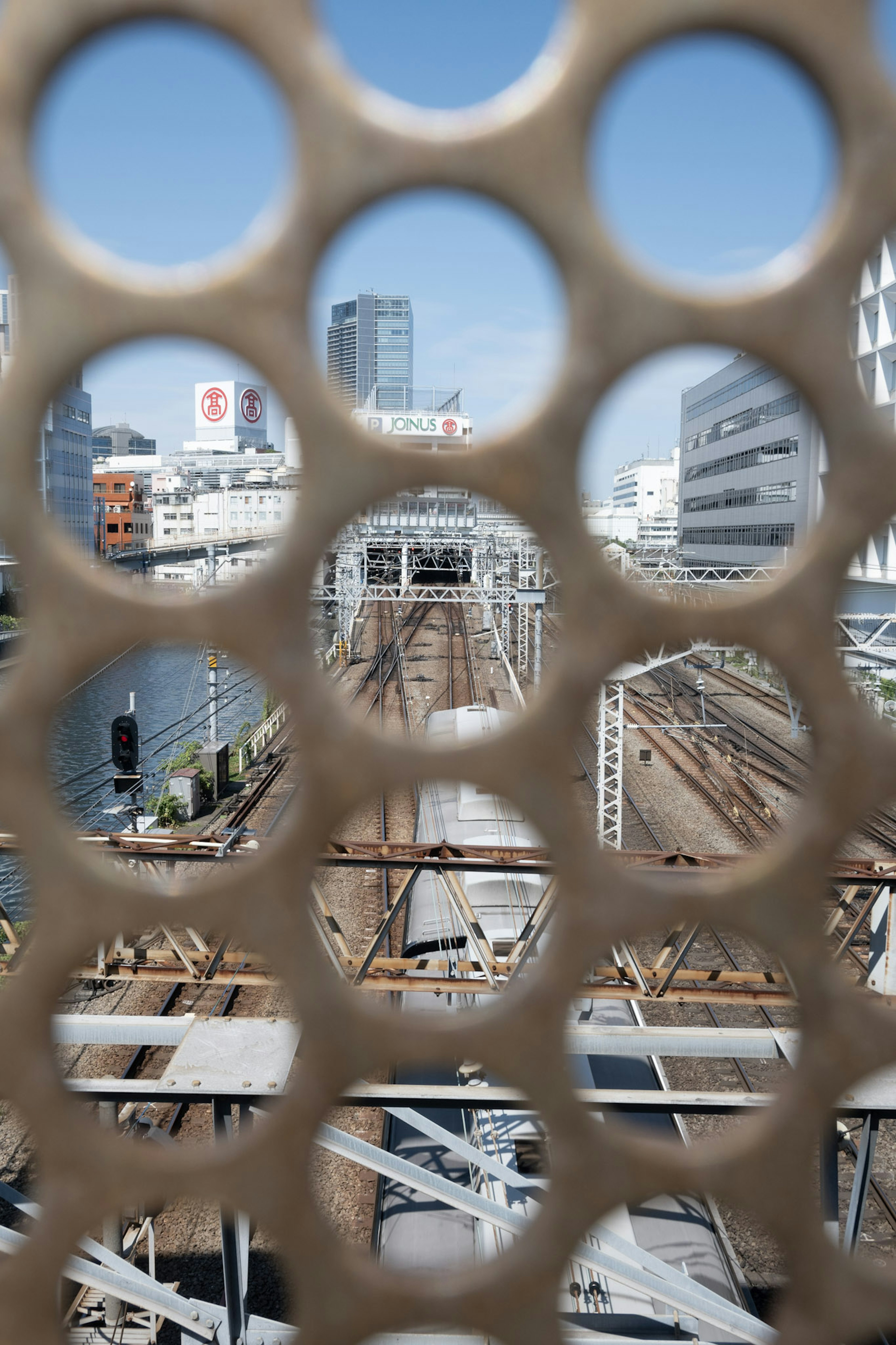 穴の開いたフェンス越しに見える鉄道と都市の風景