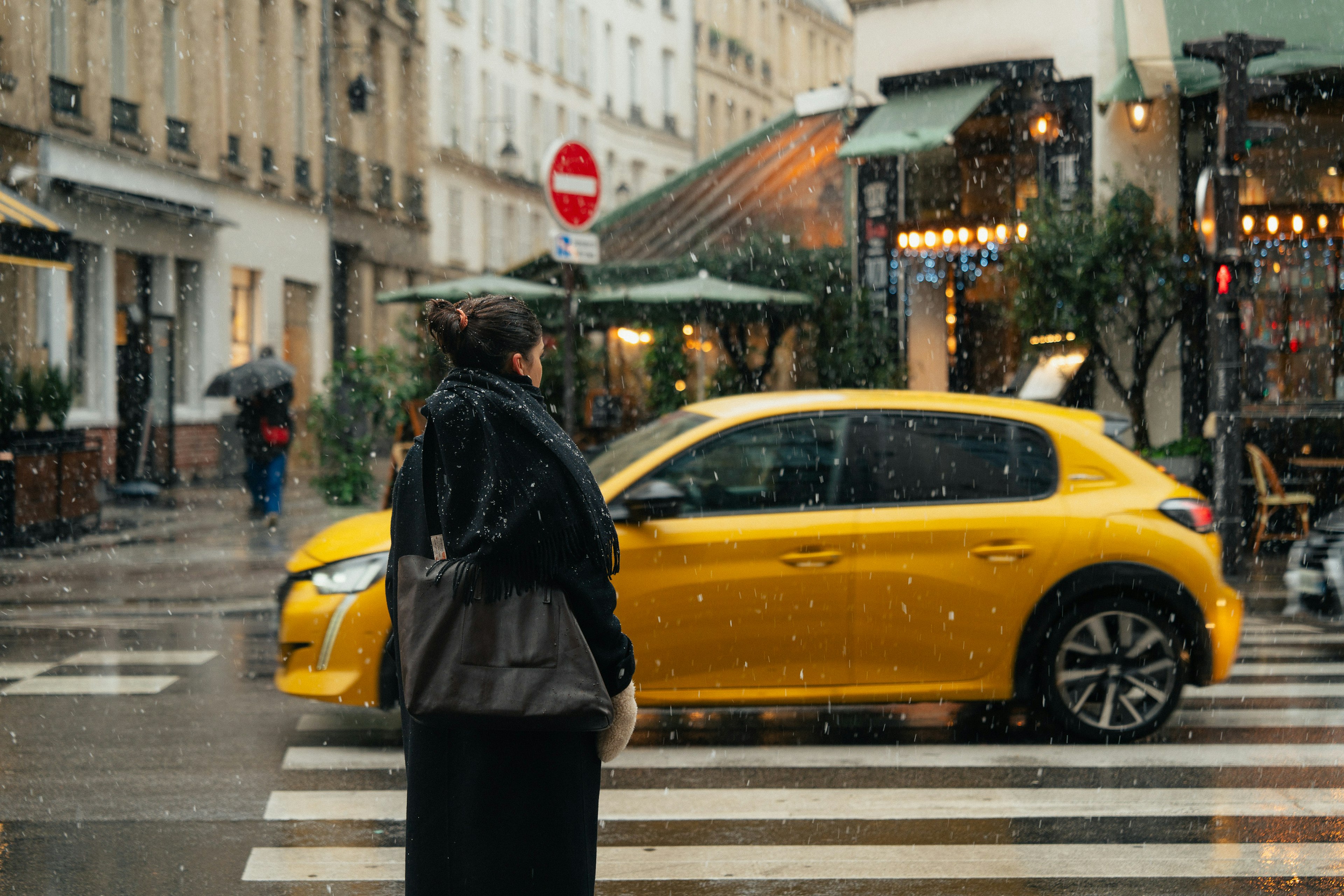 Seorang wanita menunggu di zebra cross di bawah hujan dengan mobil kuning di jalan Paris