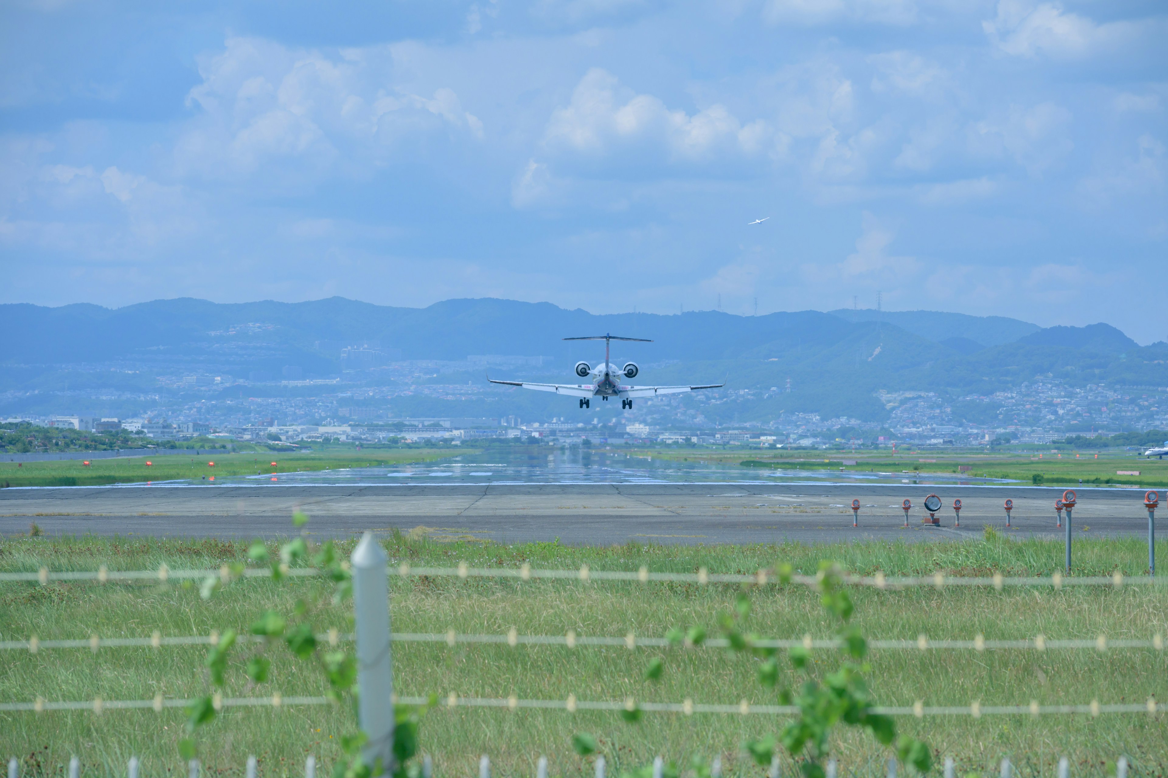 Bild eines kleinen Jets, der auf einer Landebahn landet, mit blauem Himmel und Bergen im Hintergrund