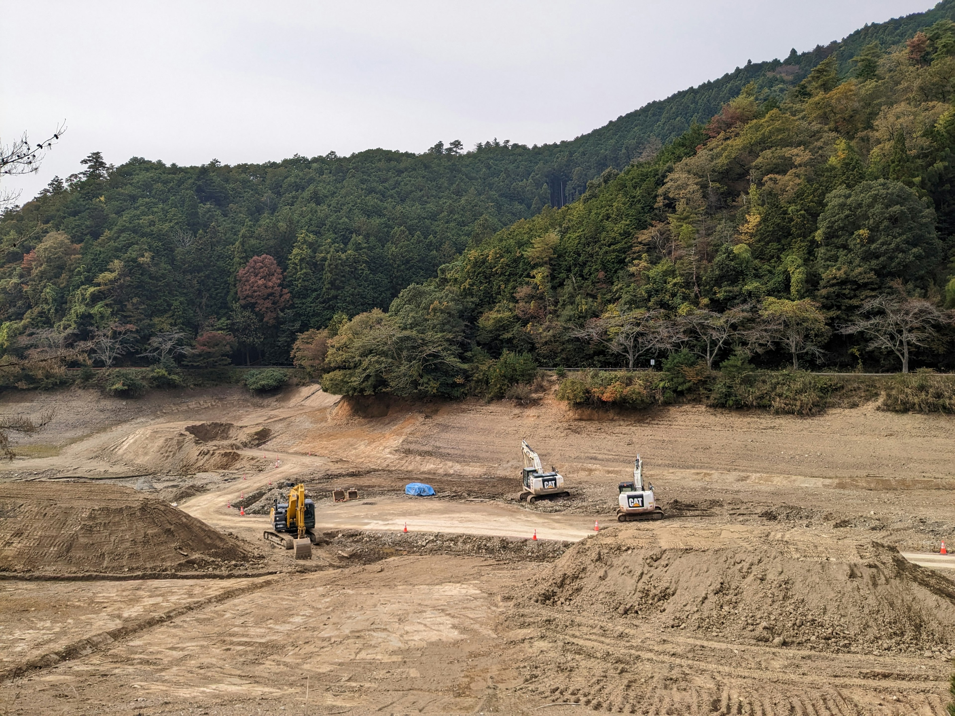 Paisaje de obra de construcción con maquinaria y montones de tierra rodeados de colinas verdes