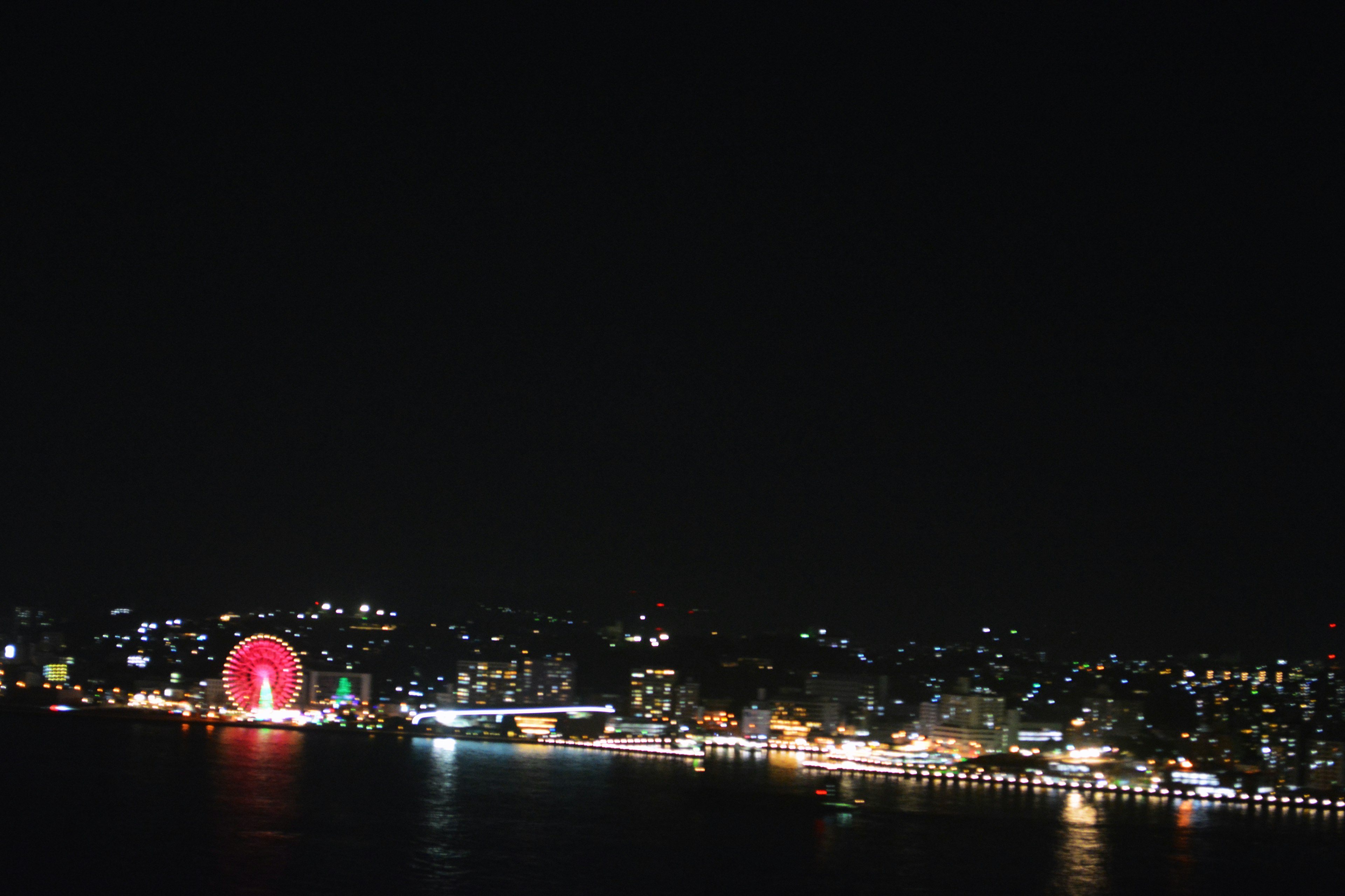 Night view of a coastline featuring a Ferris wheel and bright city lights