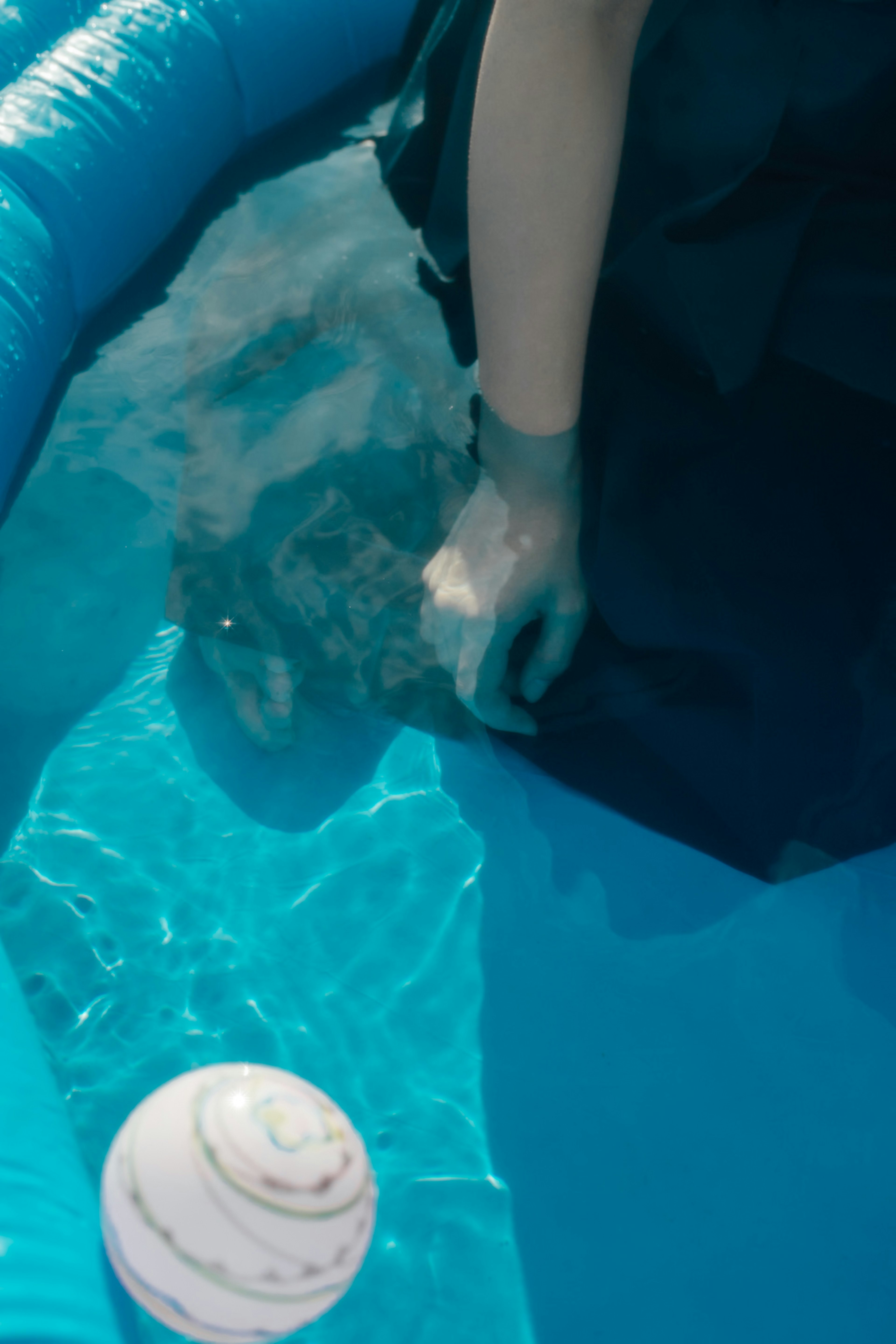 A hand submerged in blue water with a white seashell nearby