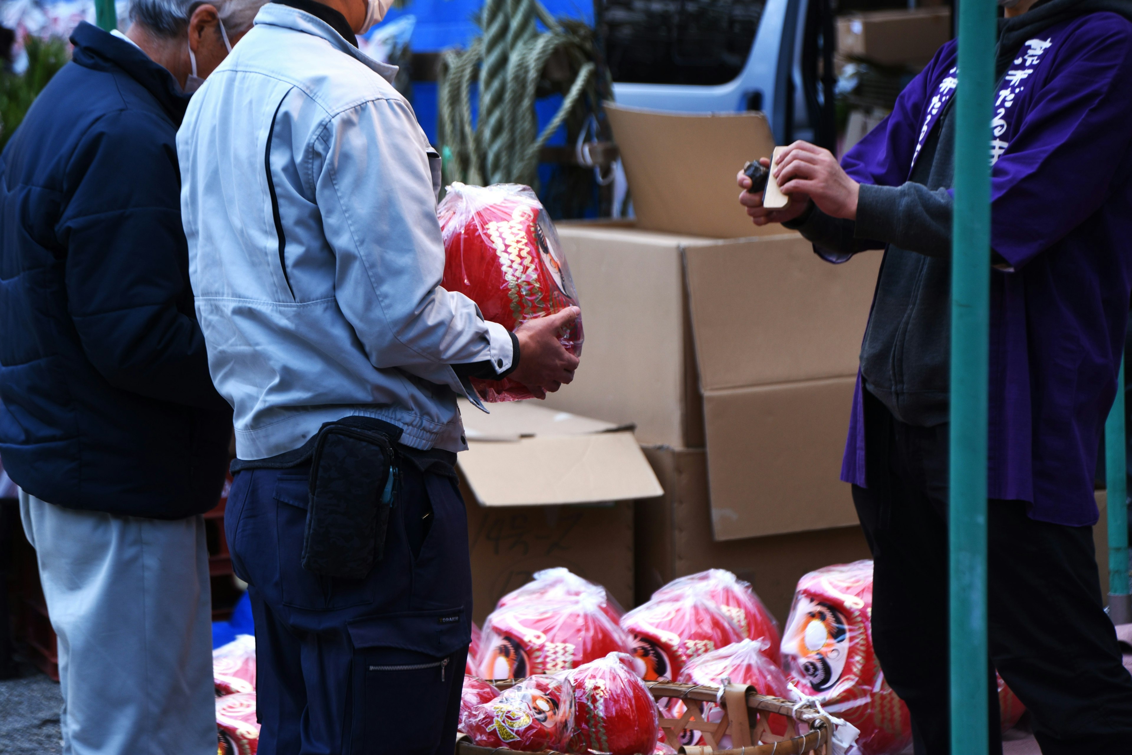 Two men at a market holding red items with boxes in the background