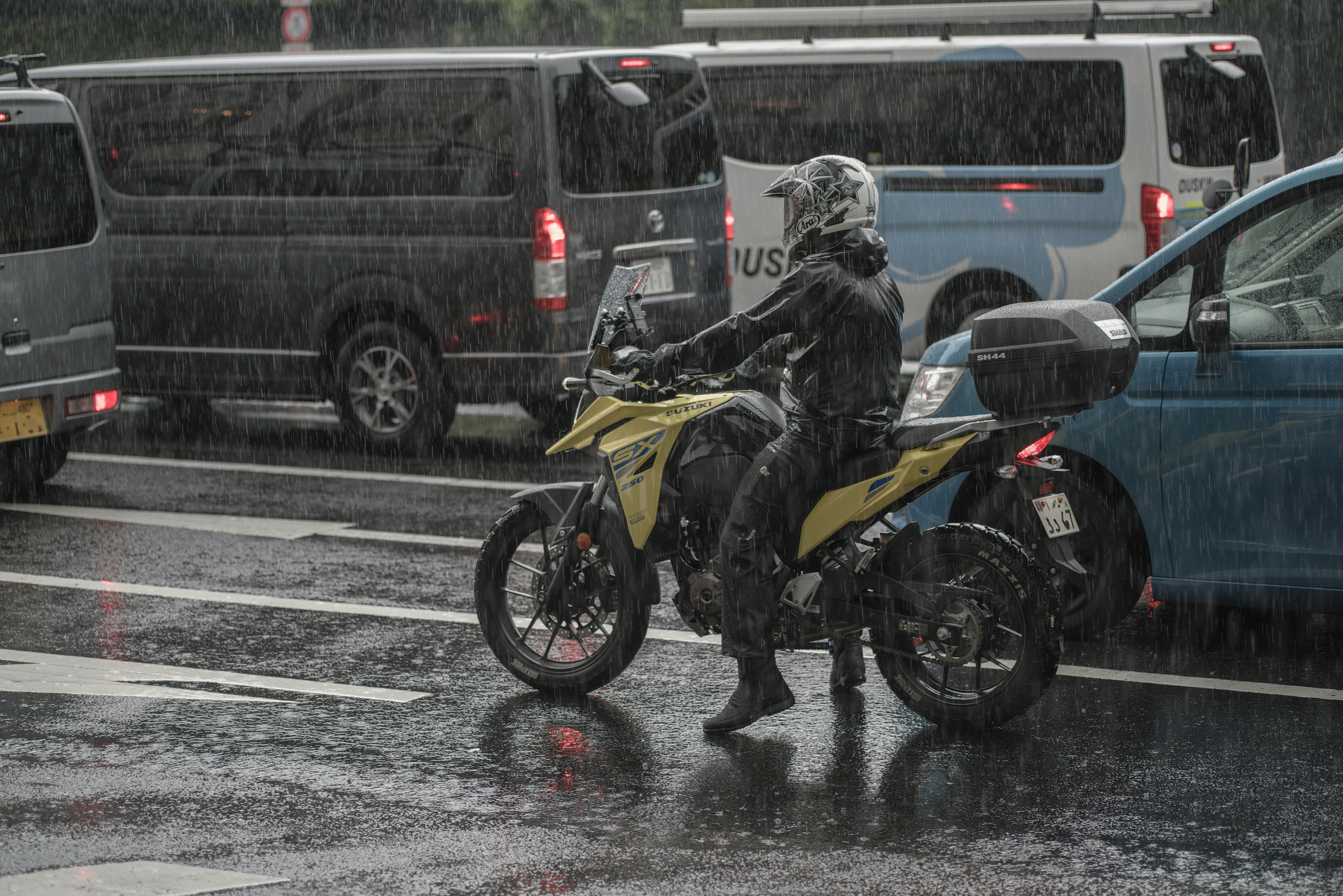 Pengendara sepeda motor di bawah hujan dikelilingi kendaraan