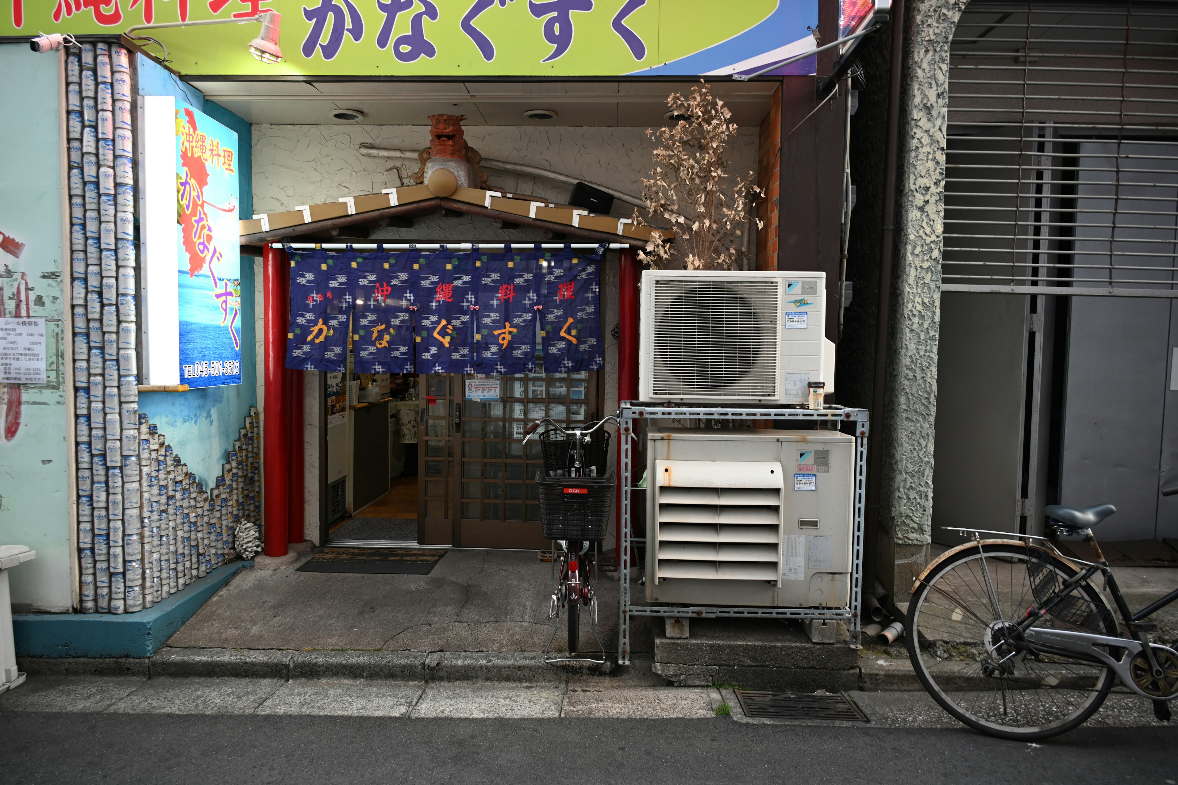 Entrada de un pequeño restaurante con un letrero brillante y un noren azul