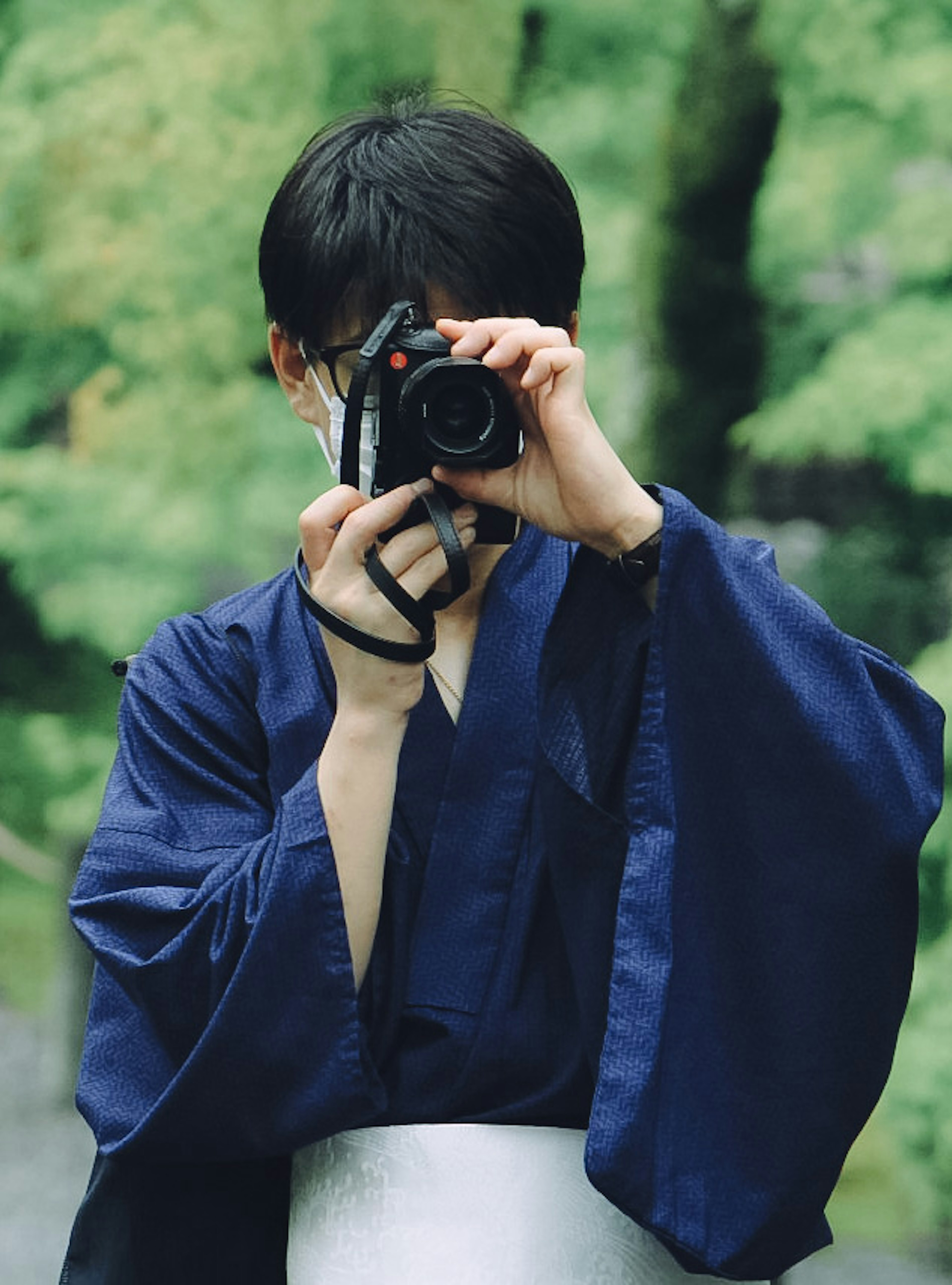 Person in blue kimono holding a camera against a green background