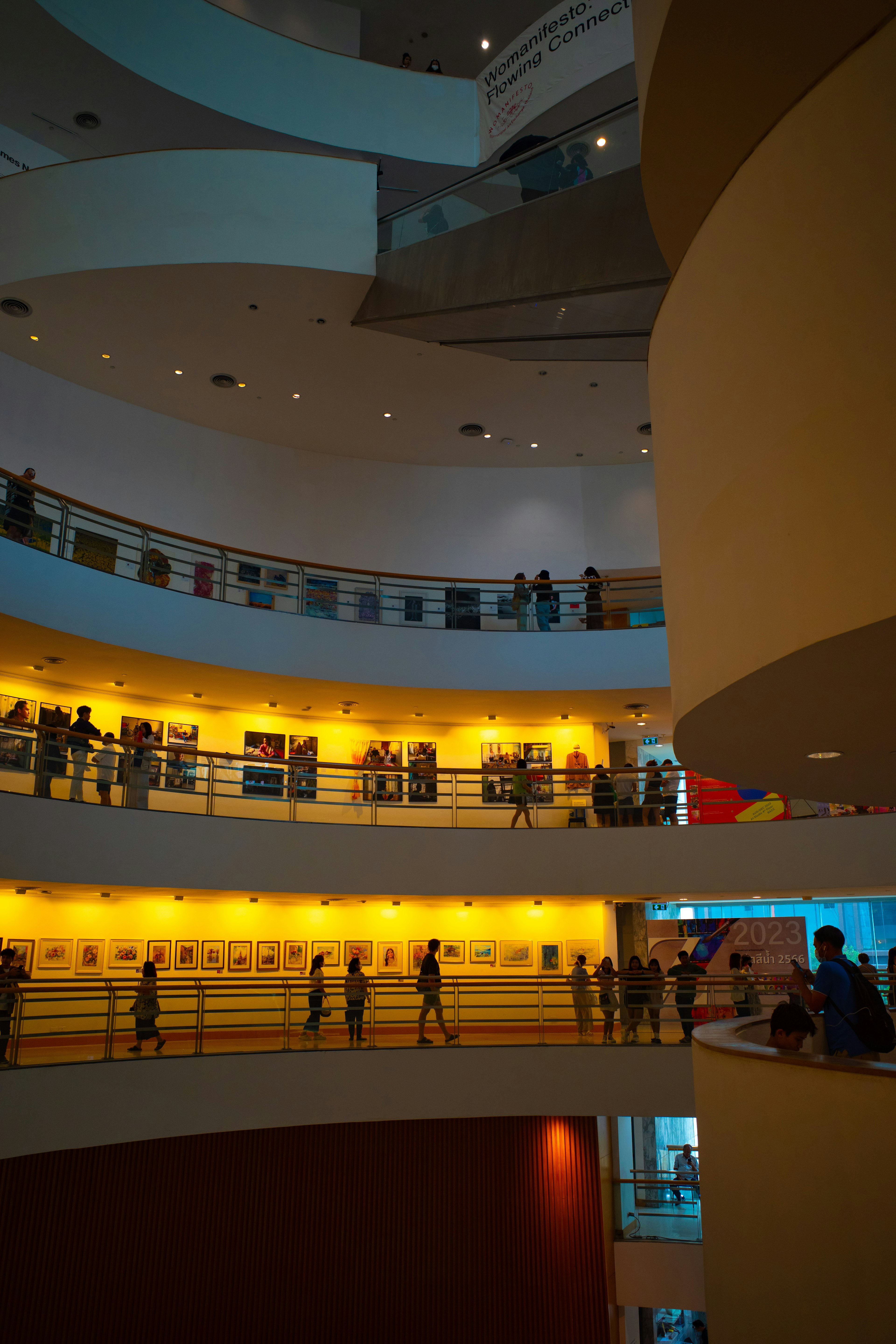 Interior of a modern art museum with tiered levels and visitors warm lighting