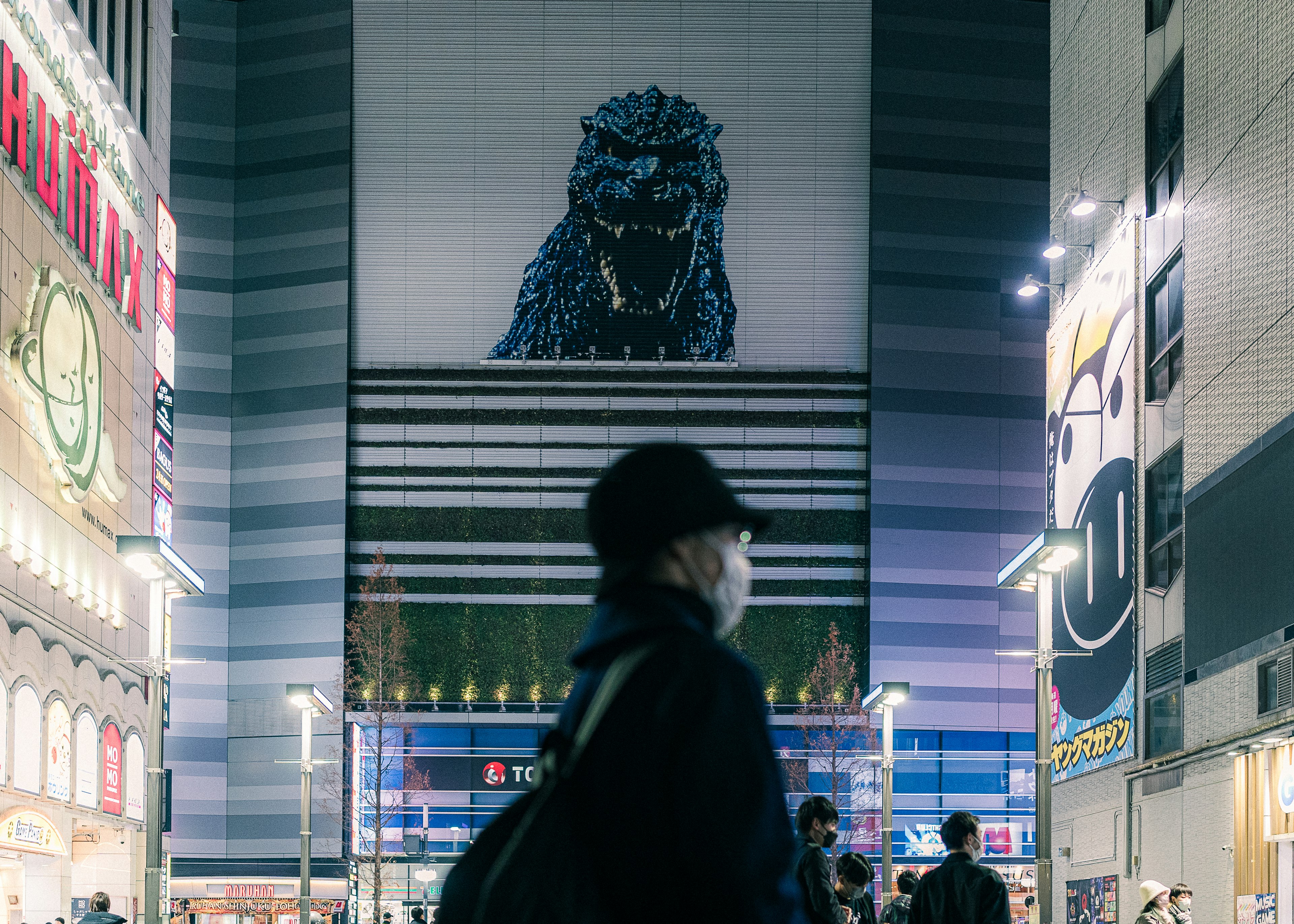 Ein riesiges Godzilla-Werbeschild in einer nächtlichen Stadtlandschaft mit Passanten