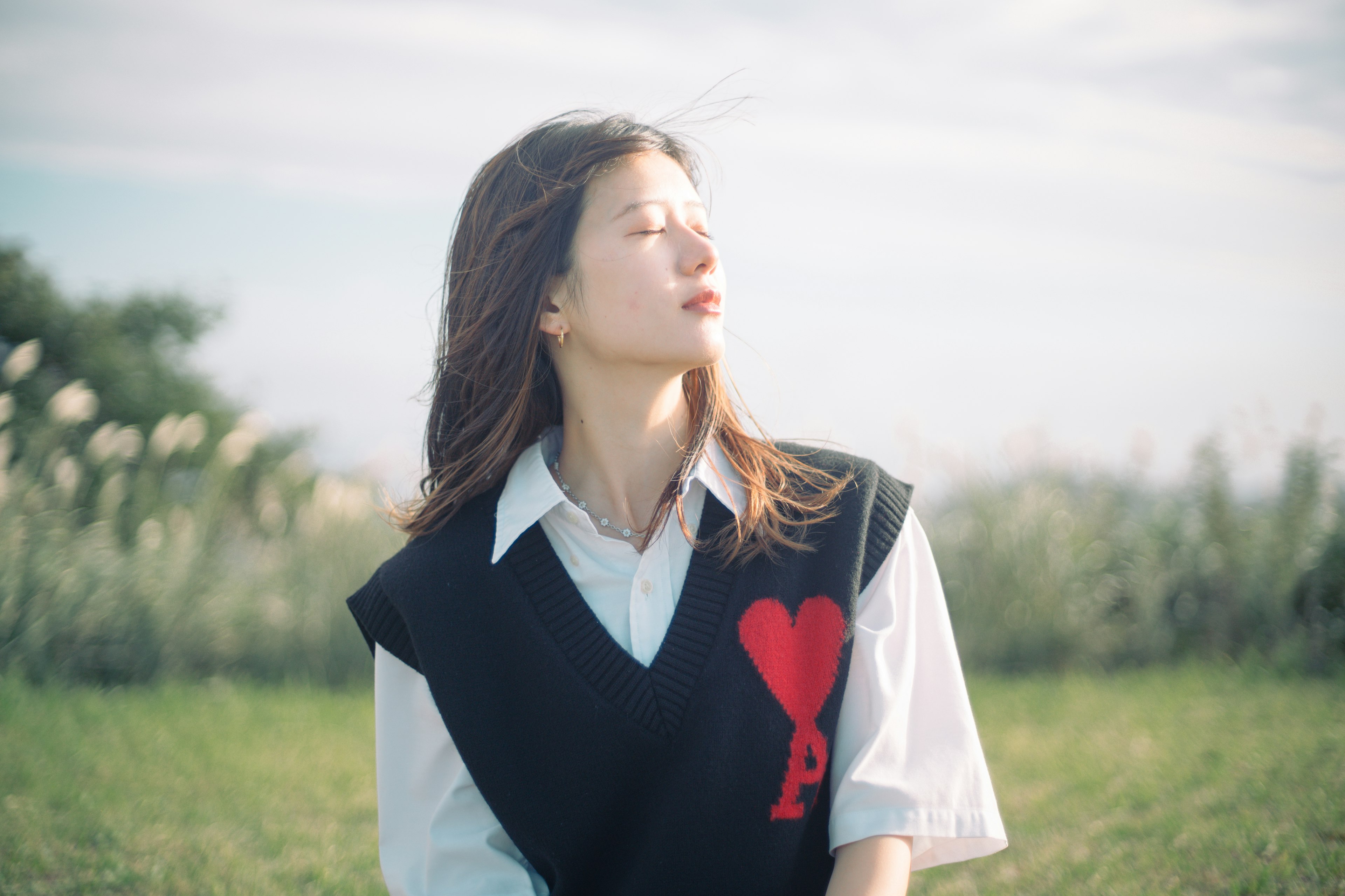 Una mujer disfrutando del sol en un campo de hierba con una camisa blanca y un chaleco negro con un diseño de corazón