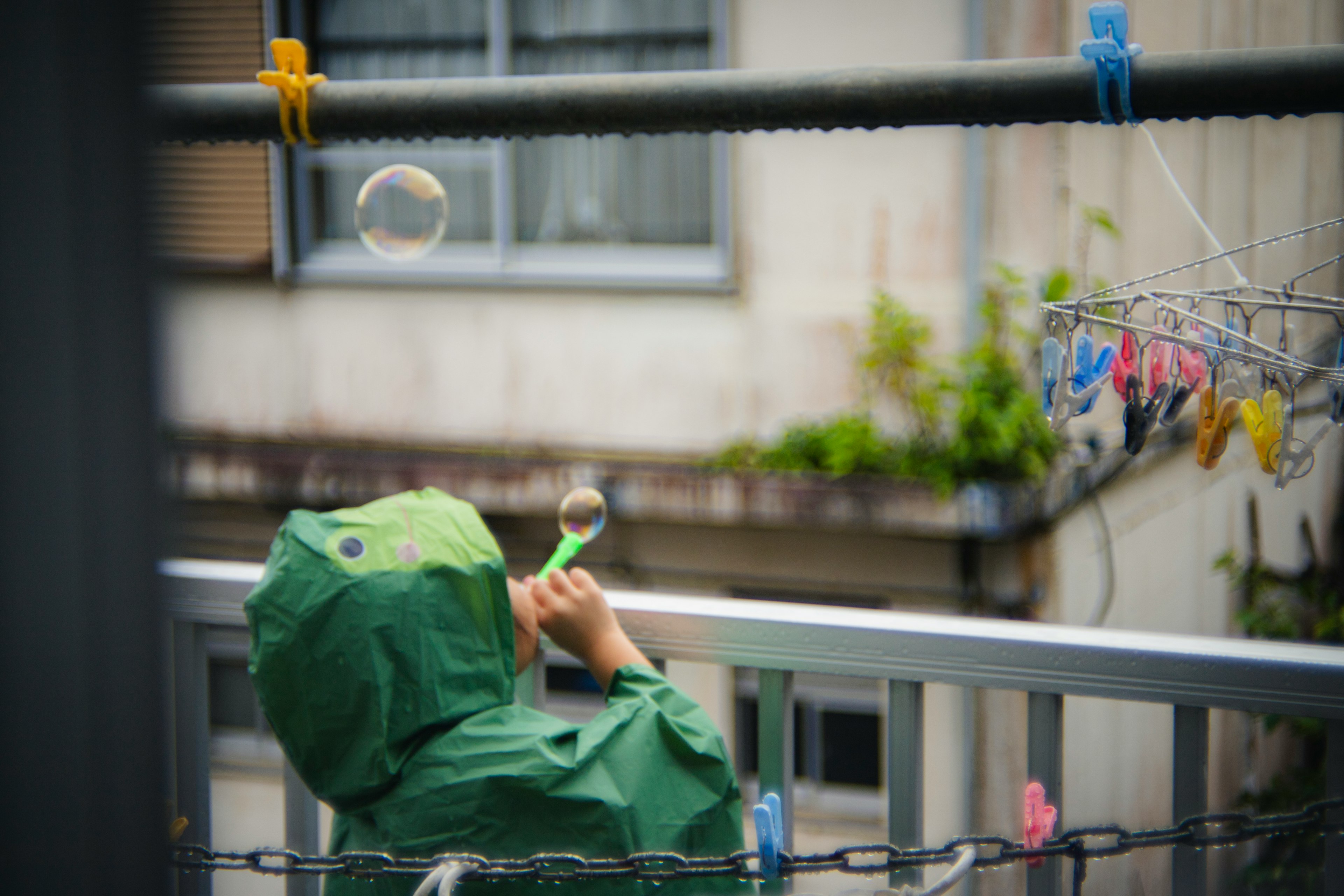 Un niño con un impermeable verde soplando burbujas en un entorno exterior