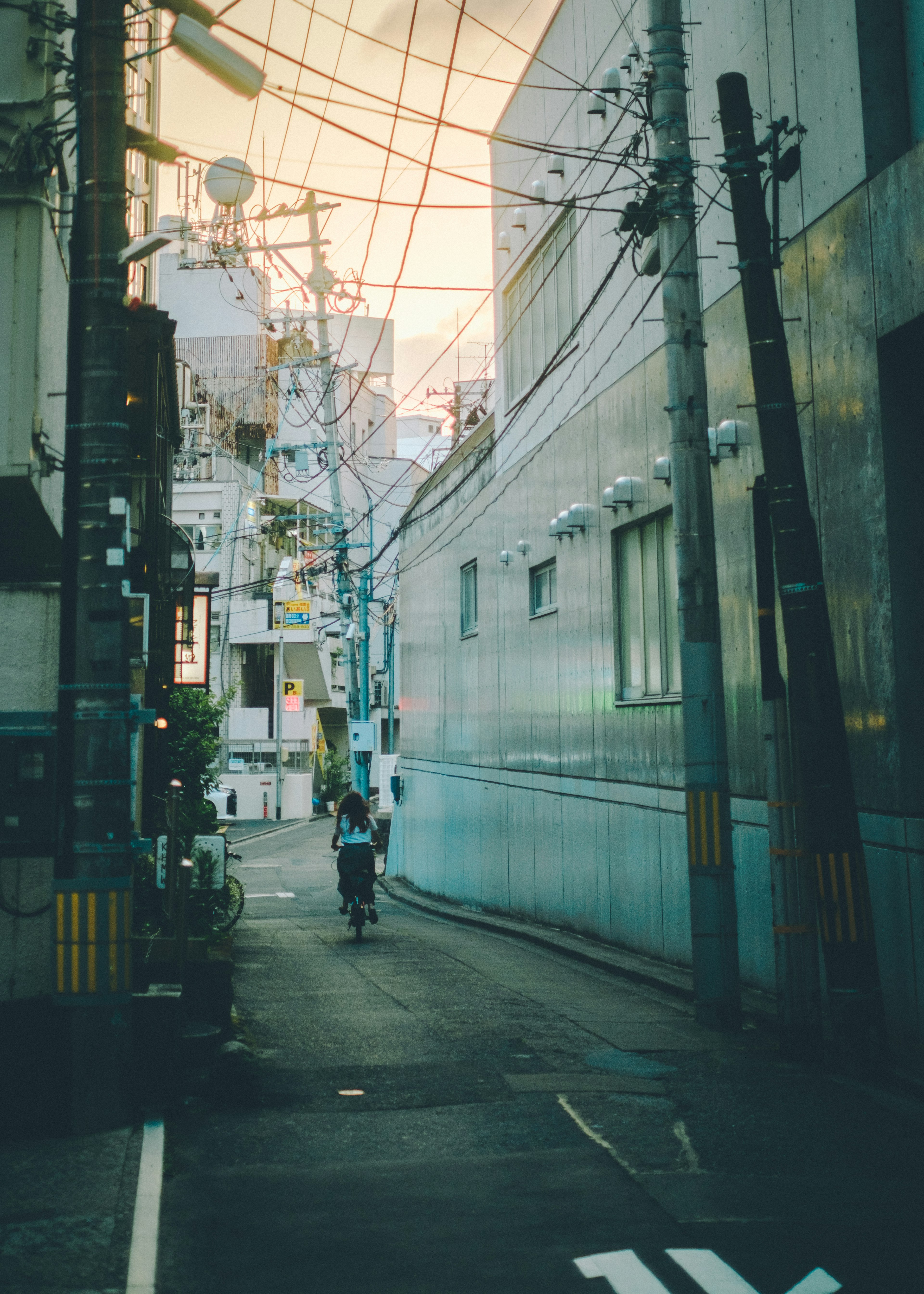 A person walking down a narrow alley surrounded by buildings and power lines