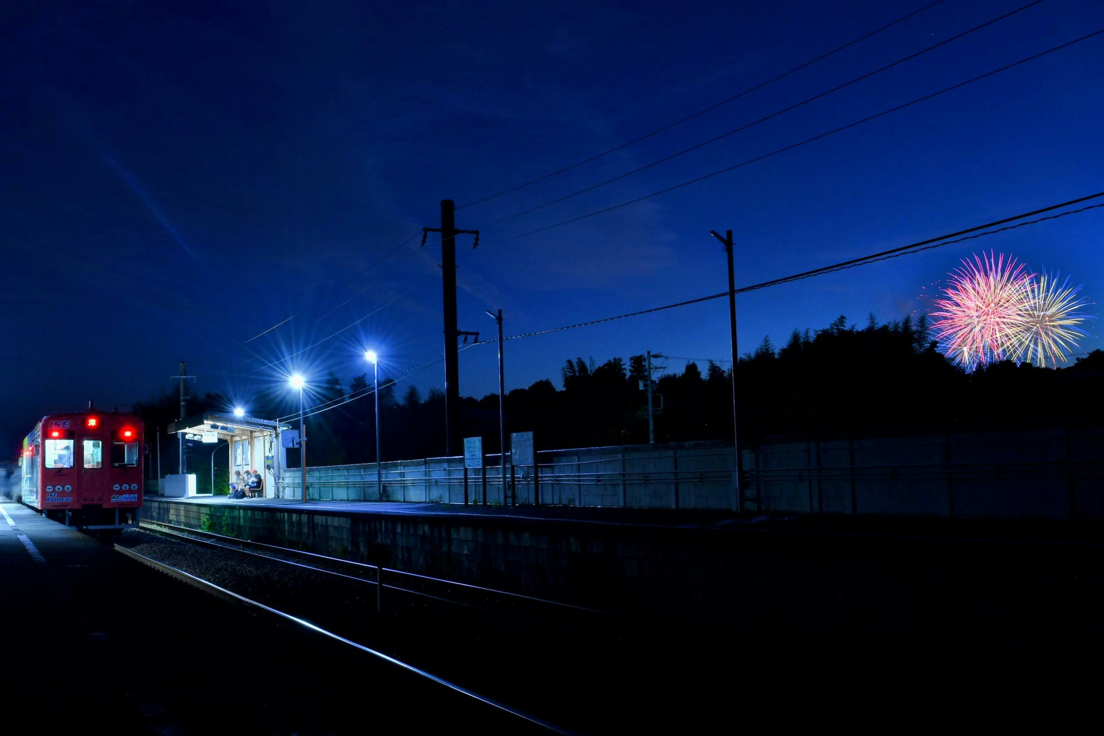 A red train at a station with fireworks in the night sky