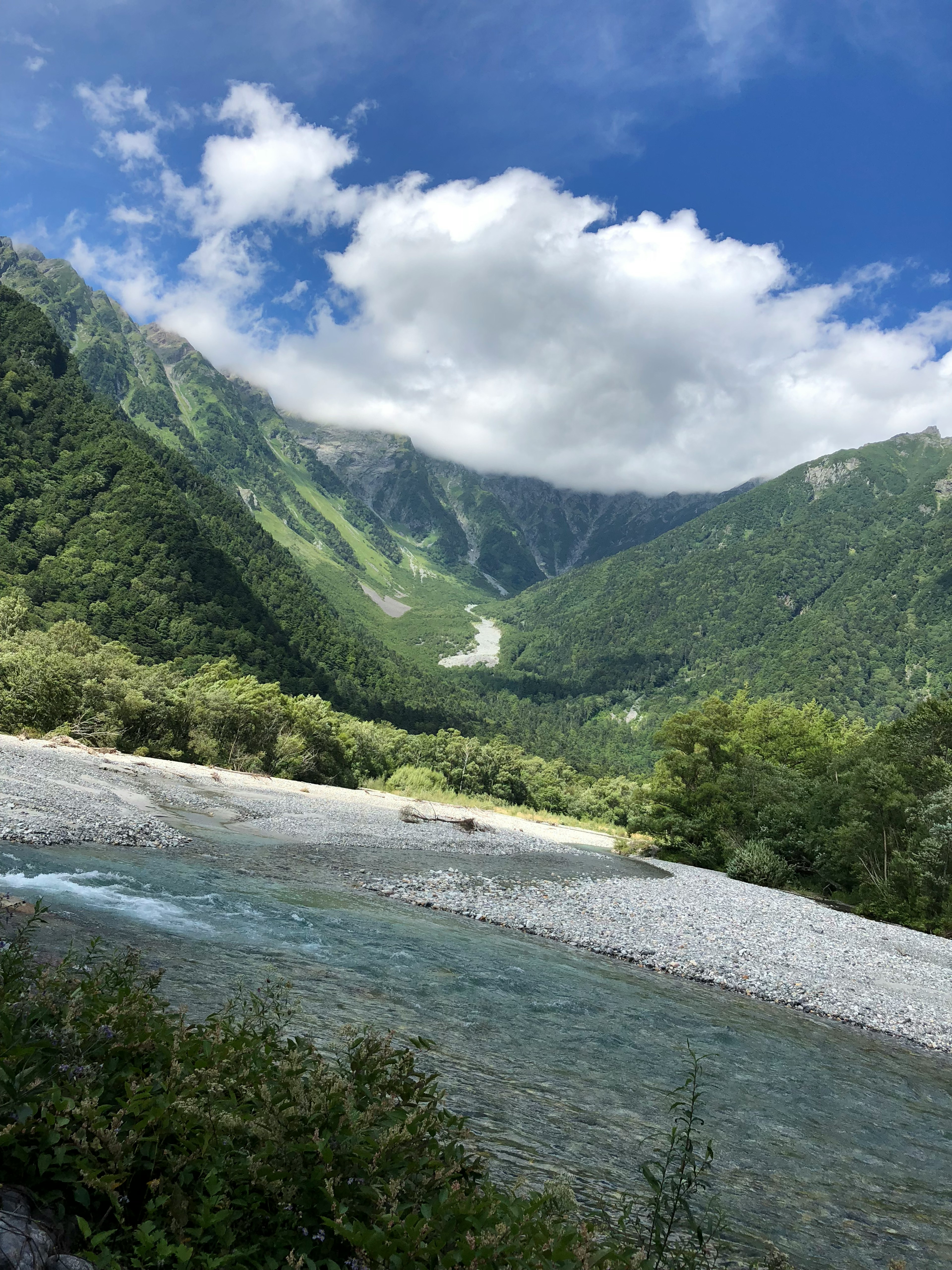 Vista escénica de montañas verdes y un río bajo un cielo brillante