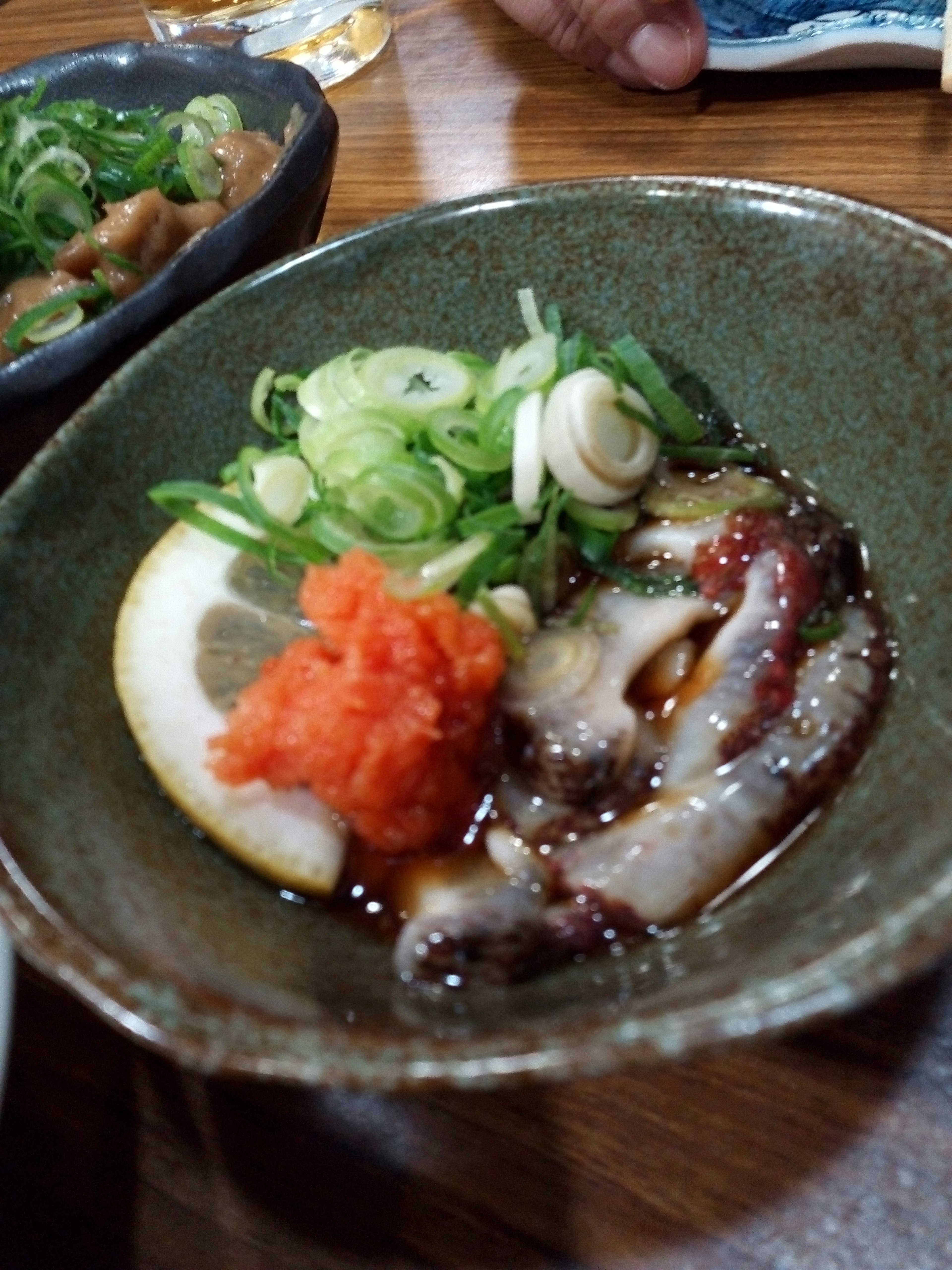 Sashimi de pulpo en rodajas con cebollín y rábano rallado en un tazón verde