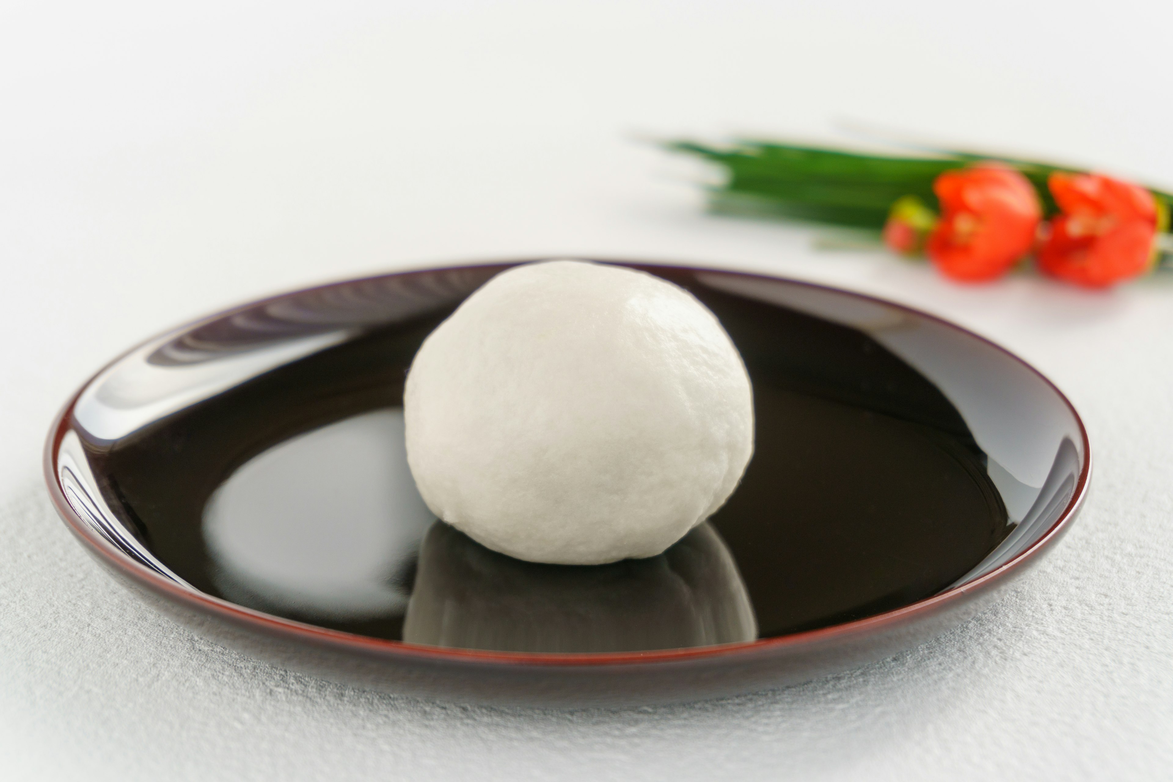 Un bollo blanco en un plato negro con cebollinos y flores naranjas al fondo