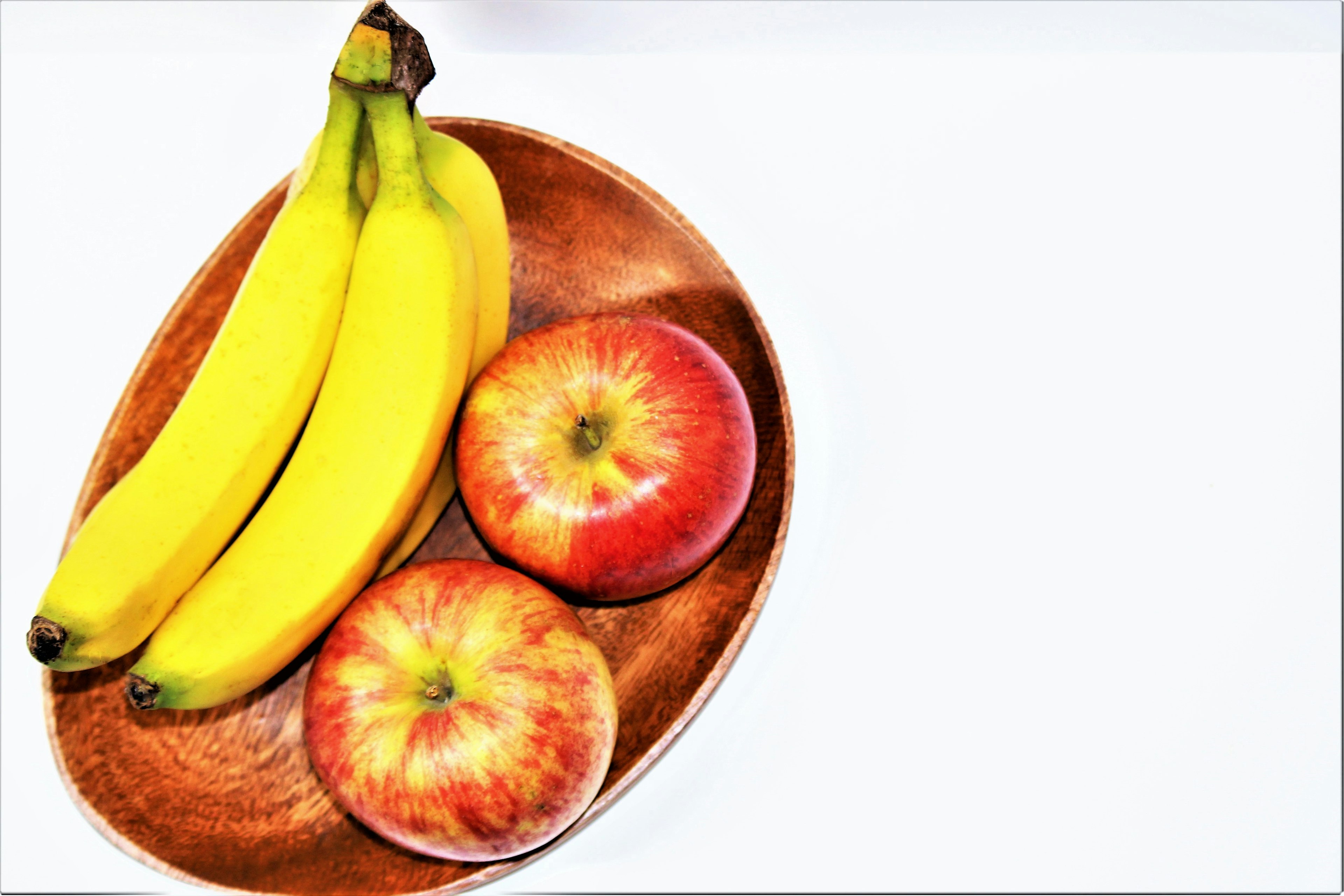 Susunan buah cerah dengan pisang dan apel di atas piring kayu