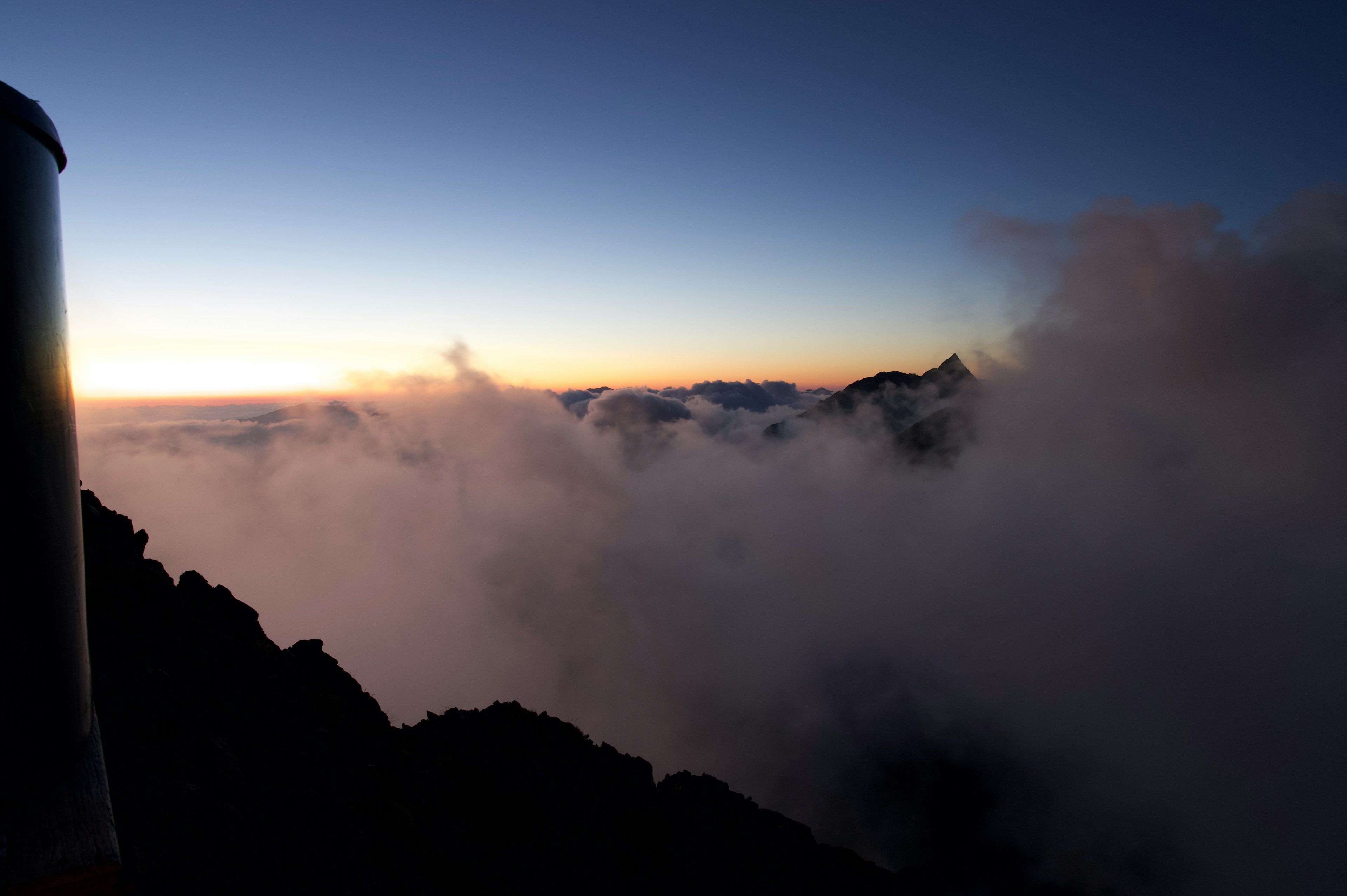 Silhouette von Bergen, die aus den Wolken gegen einen hellen Himmel auftauchen