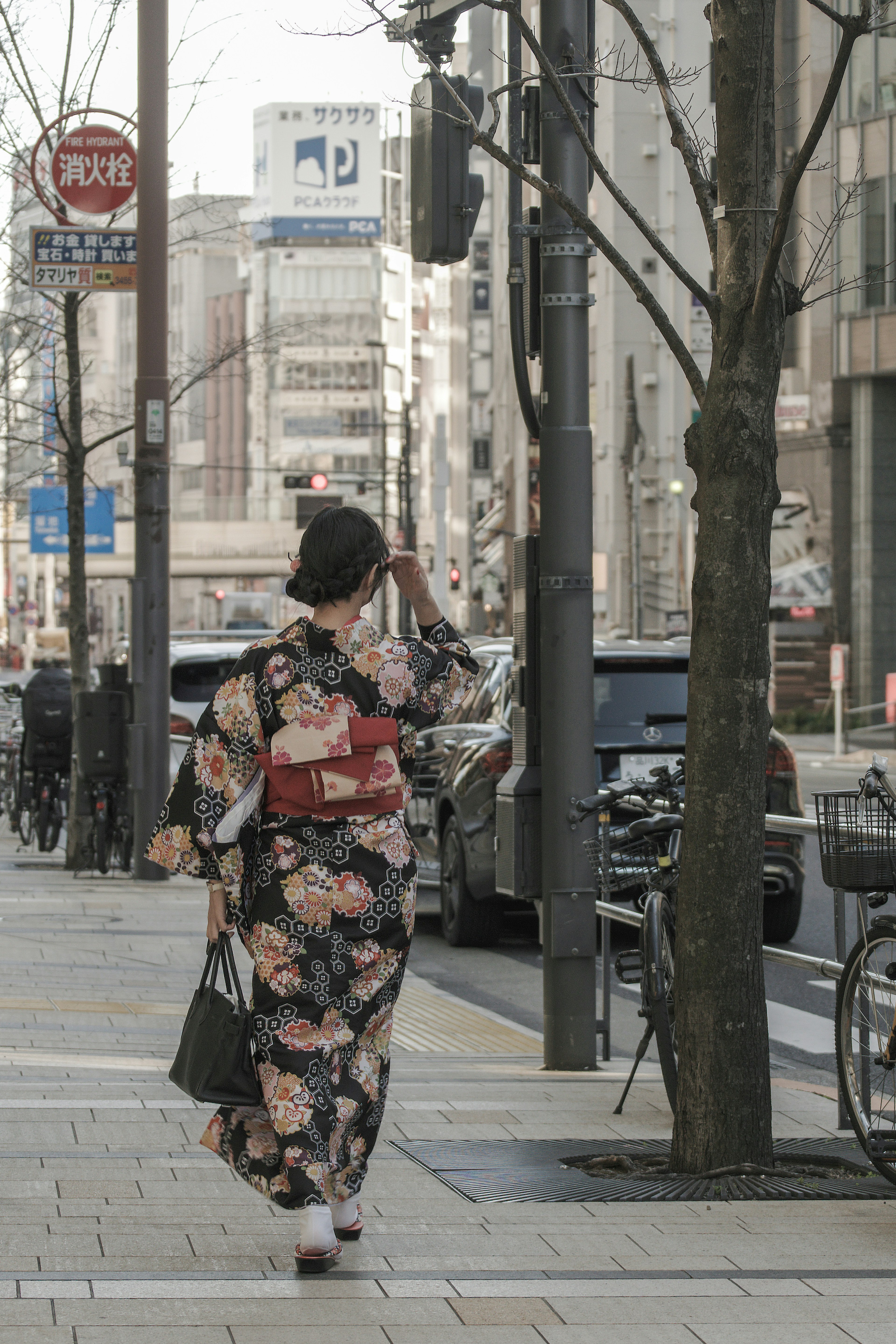 Una donna che cammina in città indossando un kimono floreale con un obi rosso